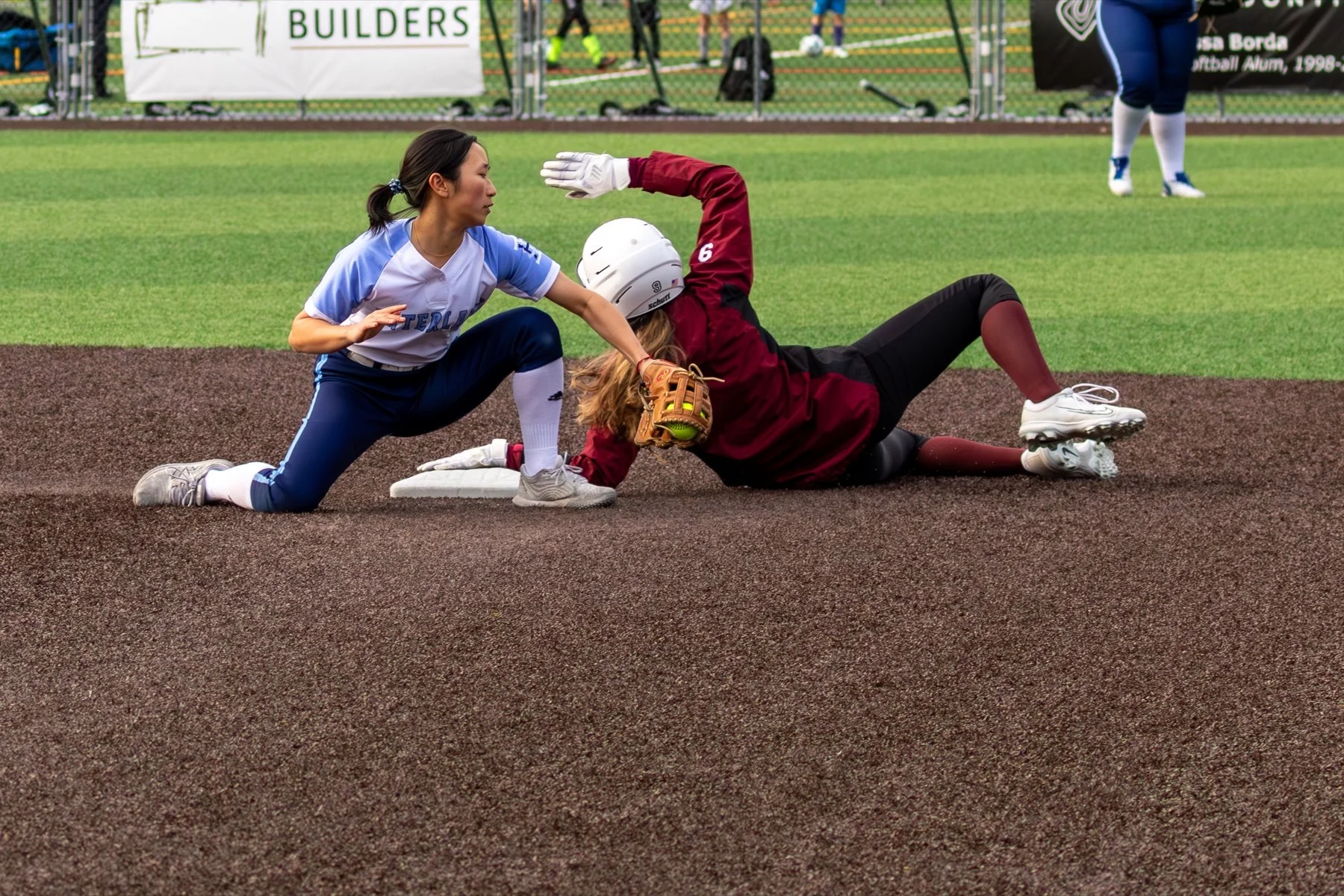 Softball runner slides toward a base as a fielder attempts a tag.