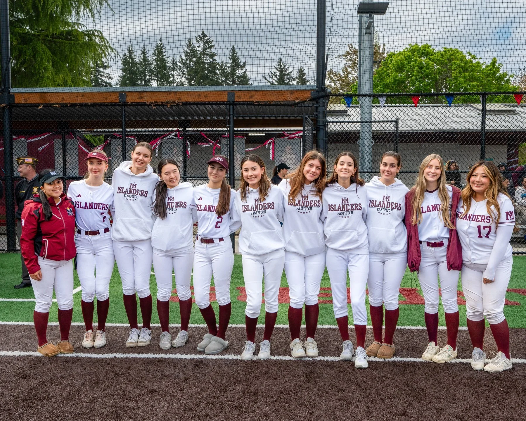 Mercer Island softball team poses in white uniforms in front of the dugout.