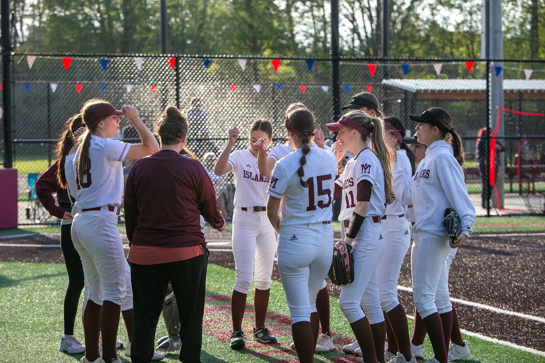 MIHS softball team gathers in a circle near the field.