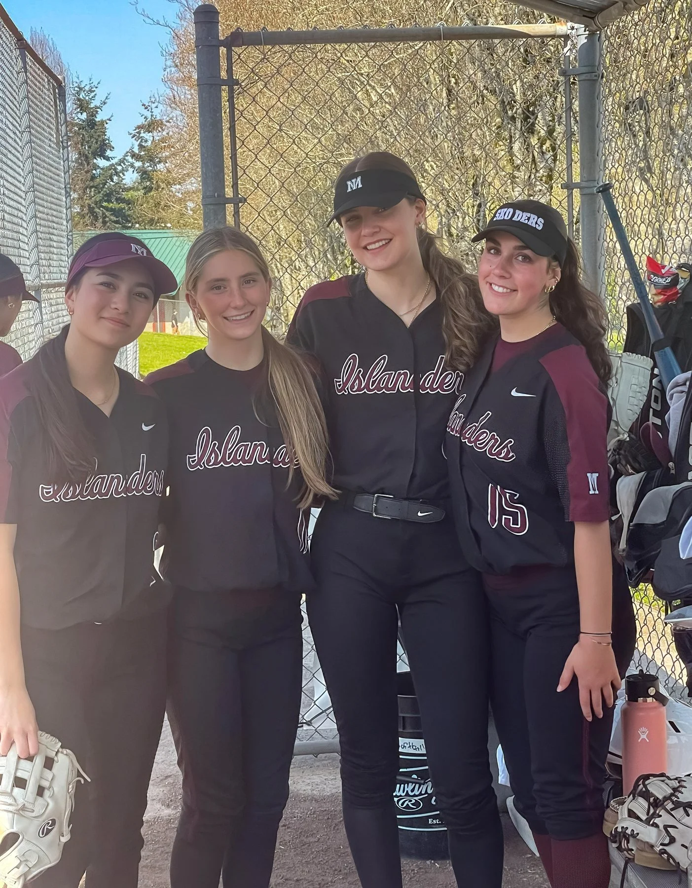 Four MIHS softball teammates pose together by the dugout.