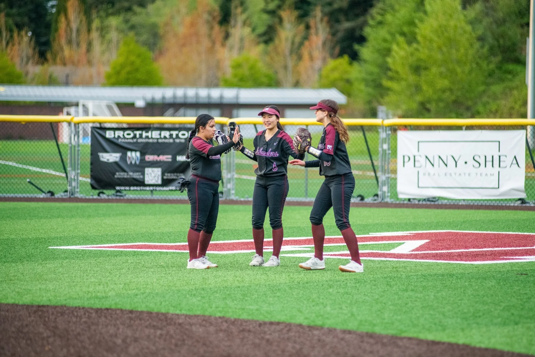 Three Islander softball players gather on the grass.