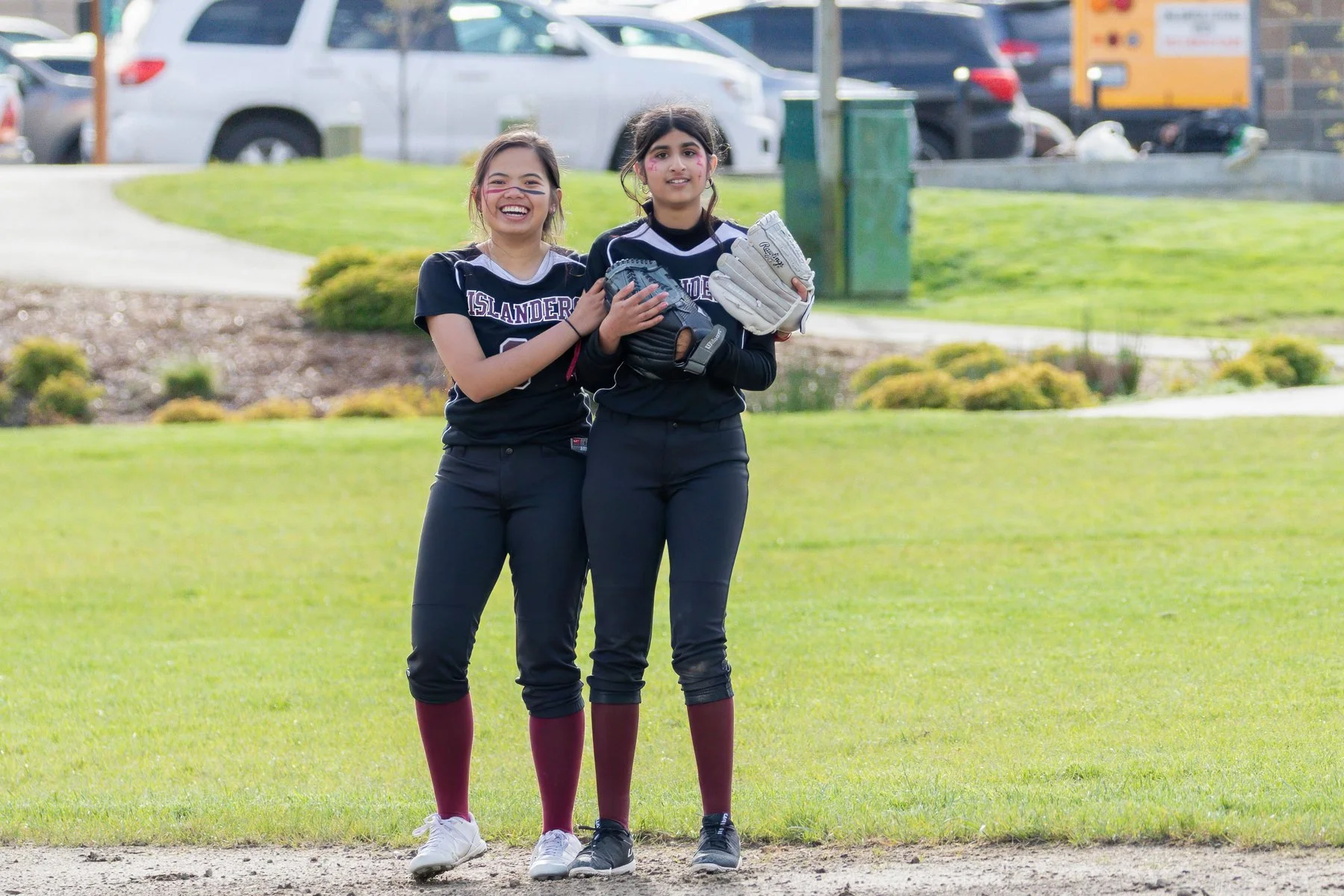 Two MIHS softball teammates smile together on the field.