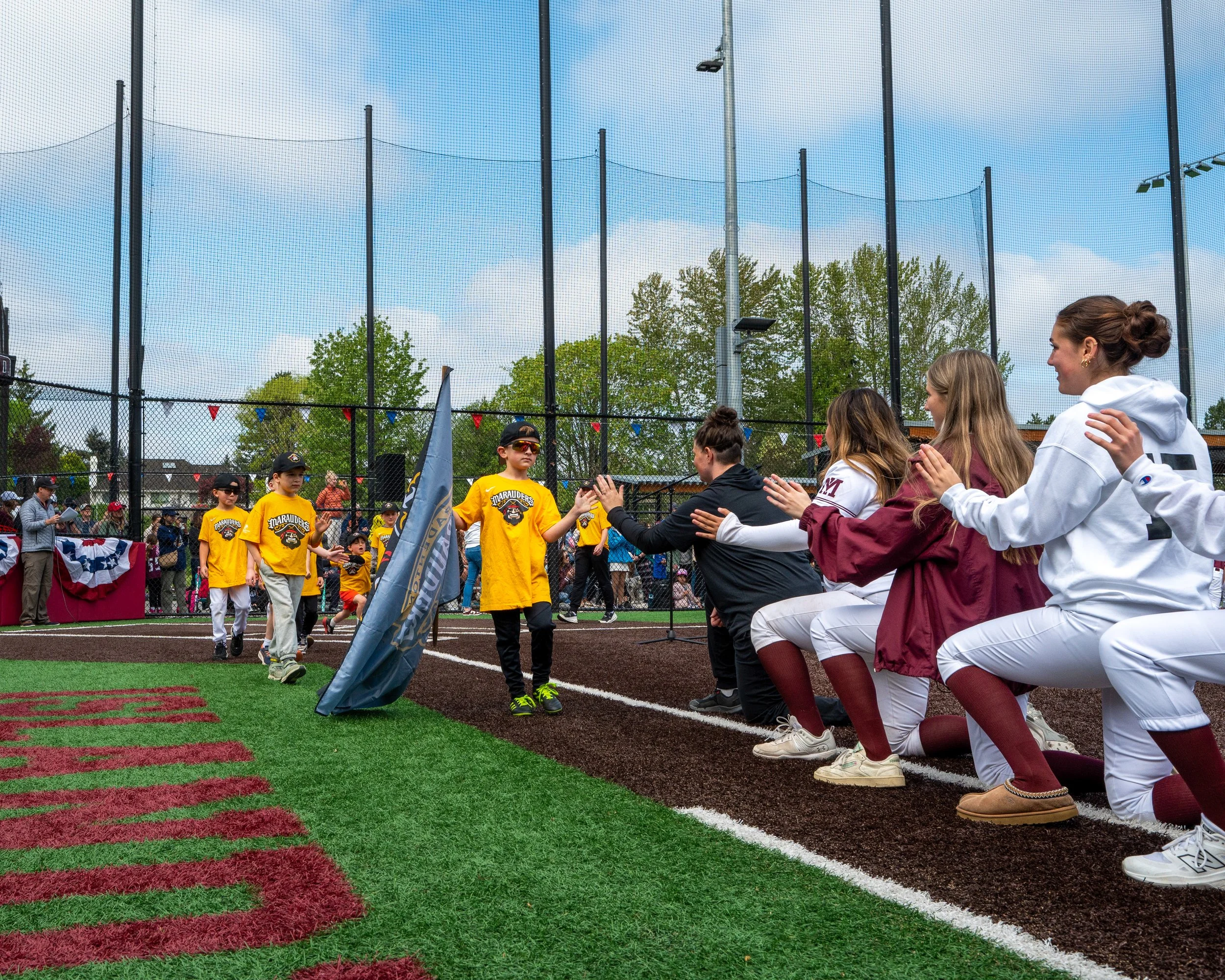 MIHS softball players greeting young Mercer Island Little League players with high-fives on the field.
