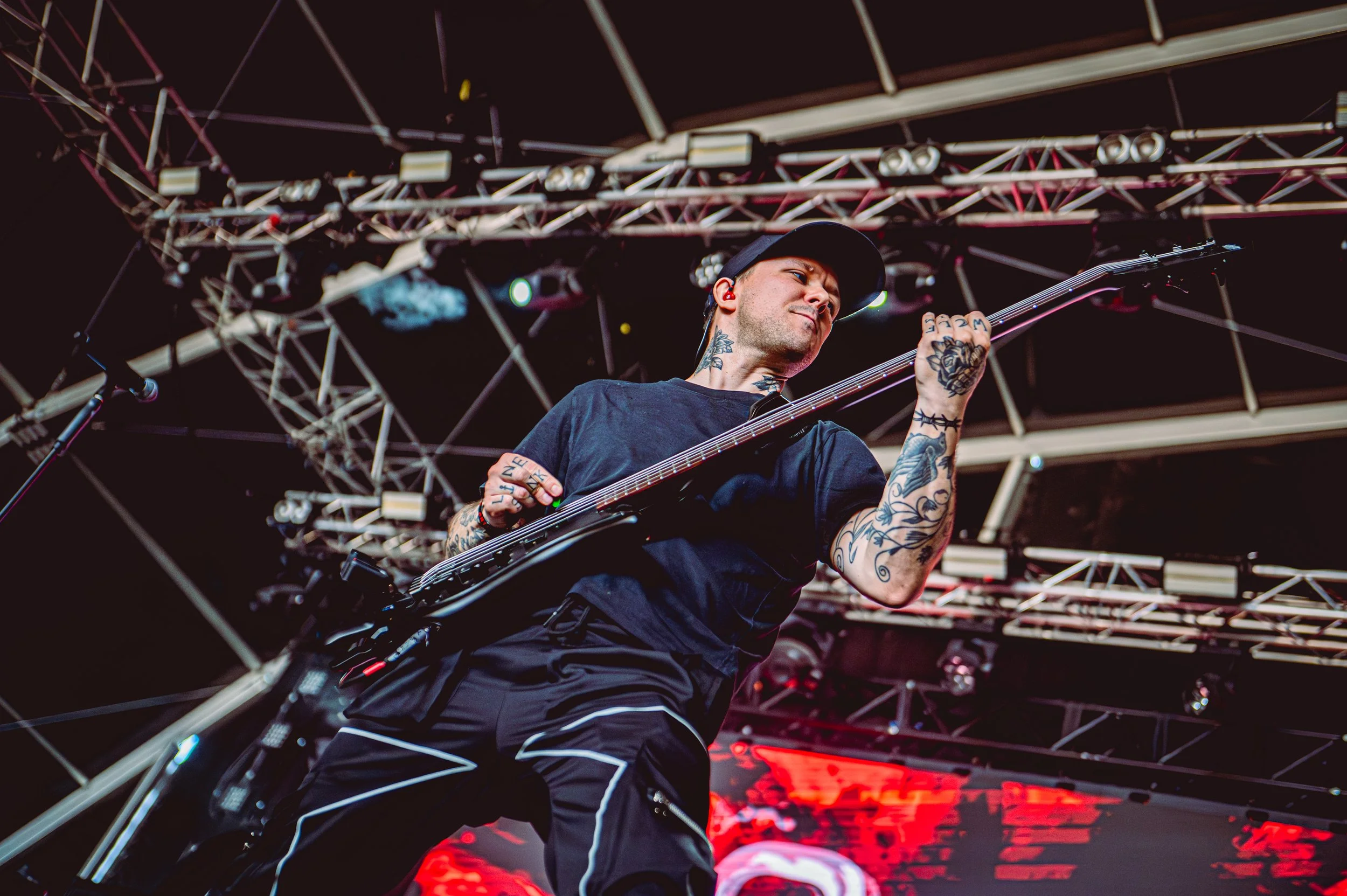 ONLY HUMAN bassist Guillaume Blanjean, with tattoos, playing electric bass guitar on stage under a complex metal truss lighting structure with a dark backdrop.