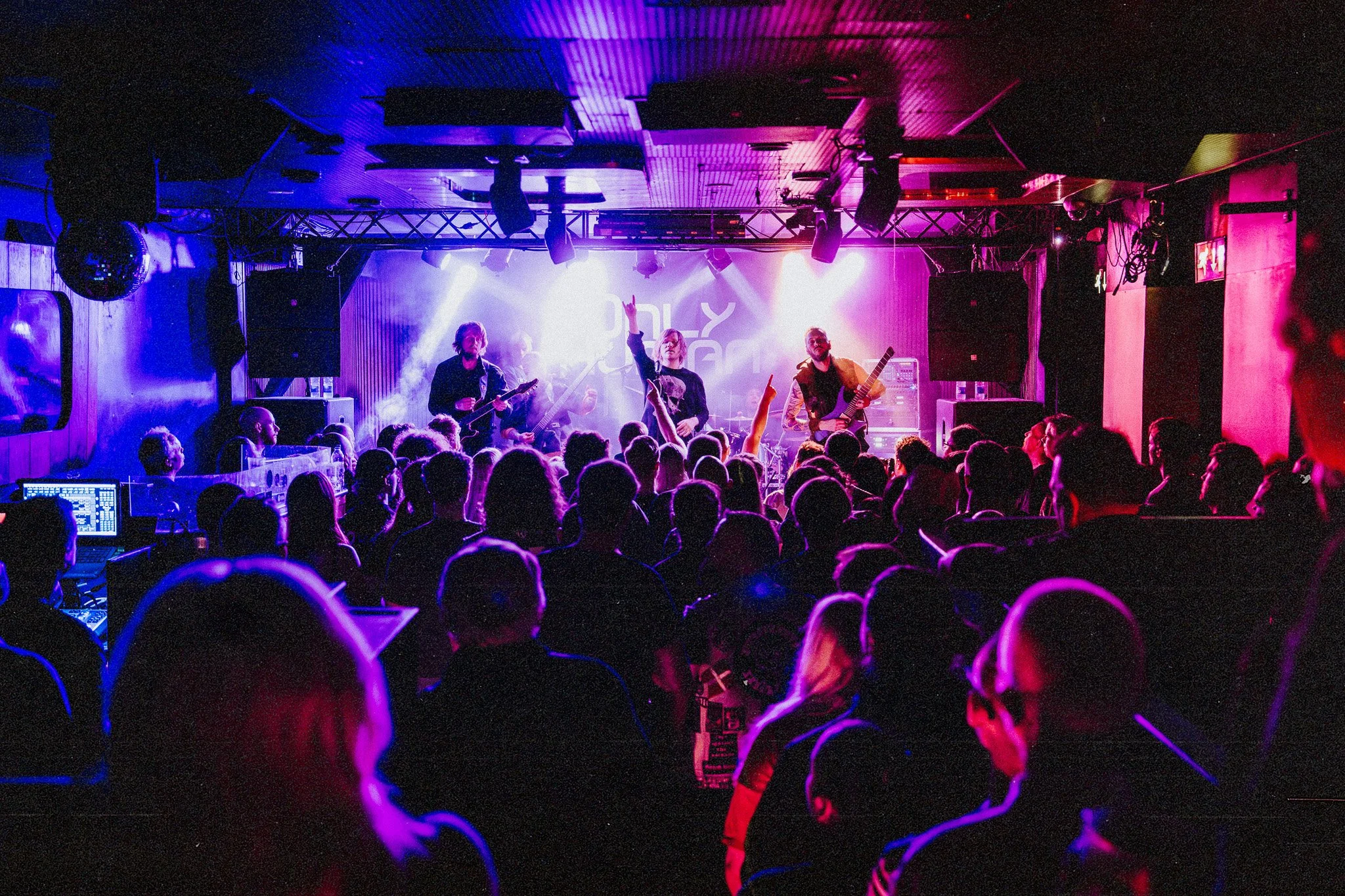 A live music concert inside a dimly lit venue with colored stage lights, the band ONLY HUMAN performing on stage, and an audience watching.