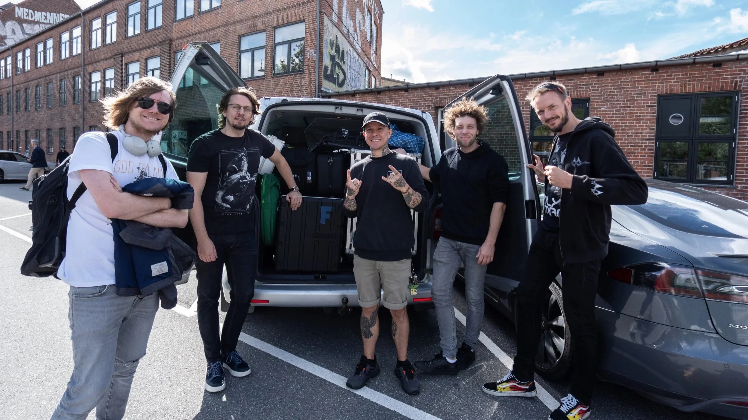 All five members of ONLY HUMAN, standing by the back of an open packed van smiling for the camera on a bright sunny day with a blue sky. Left-to-right: Patrick, Martin, Guillaume, Andreas, Jack.