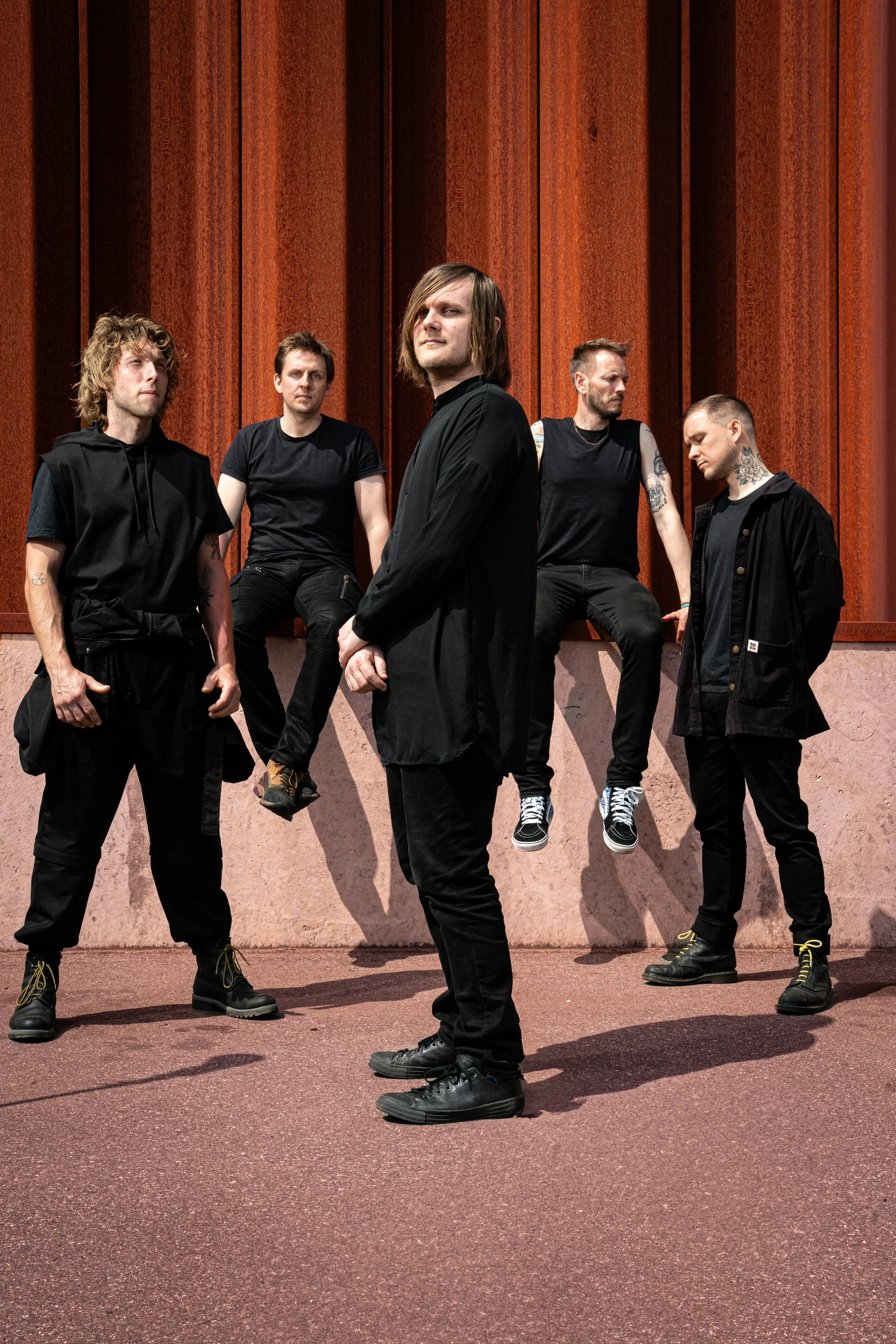 Press photo of the five members of ONLY HUMAN posing against a rust-colored wall with shadows on the ground. Left-to-right: Andreas, Martin, Patrick, Jack, Guillaume. 