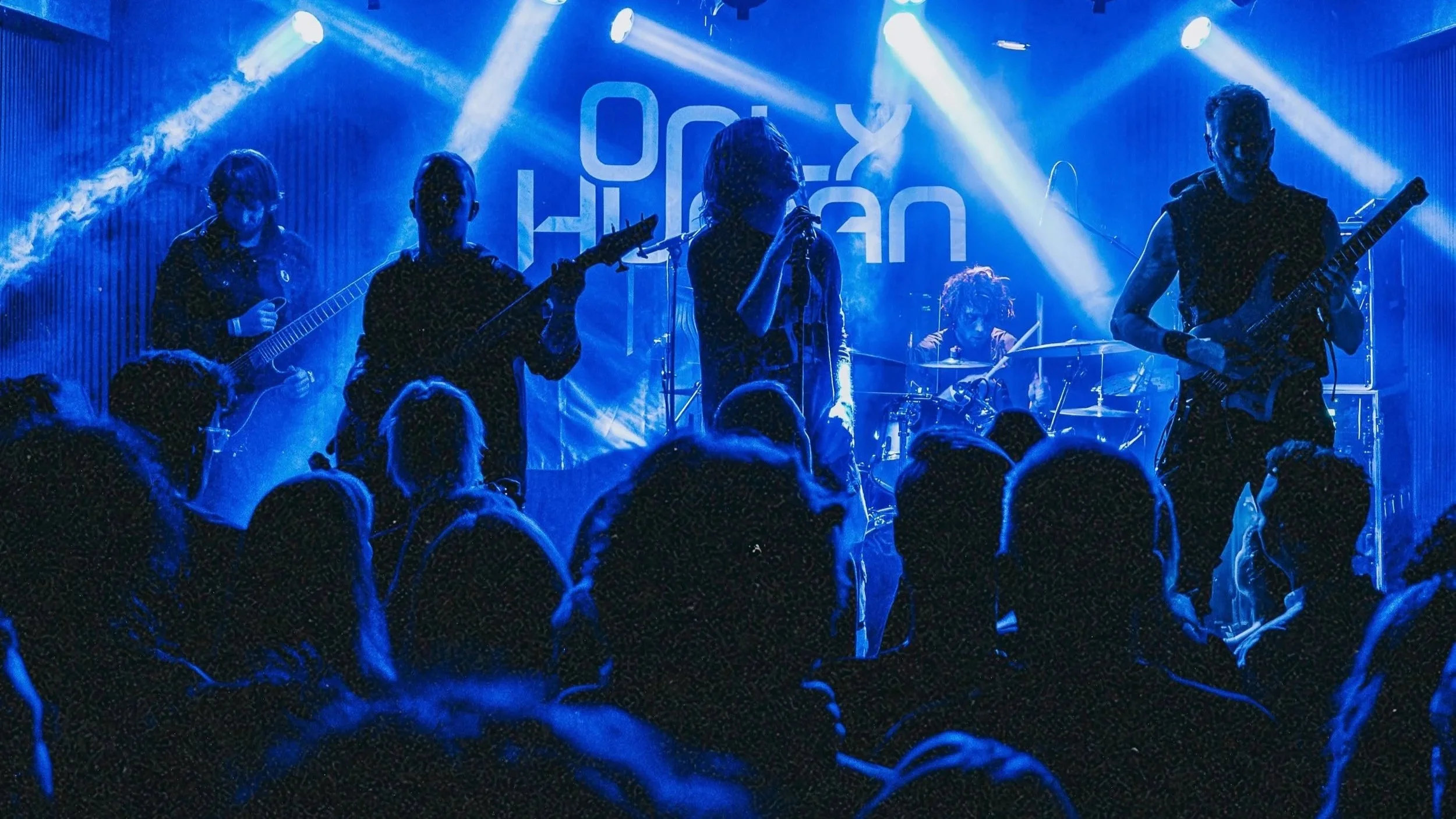 All members of ONLY HUMAN performing on stage silhouetted in blue light, crowd watching in front.