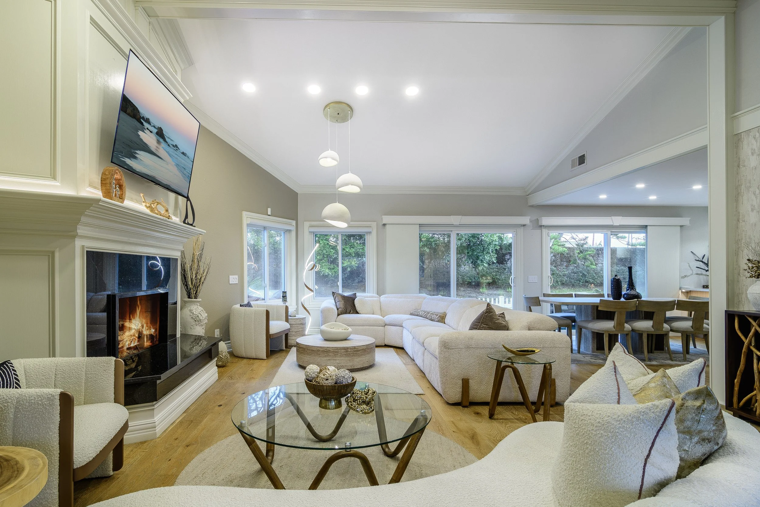 Light-filled contemporary living room with neutral furnishings, a fireplace, modern lighting, and expansive garden views.