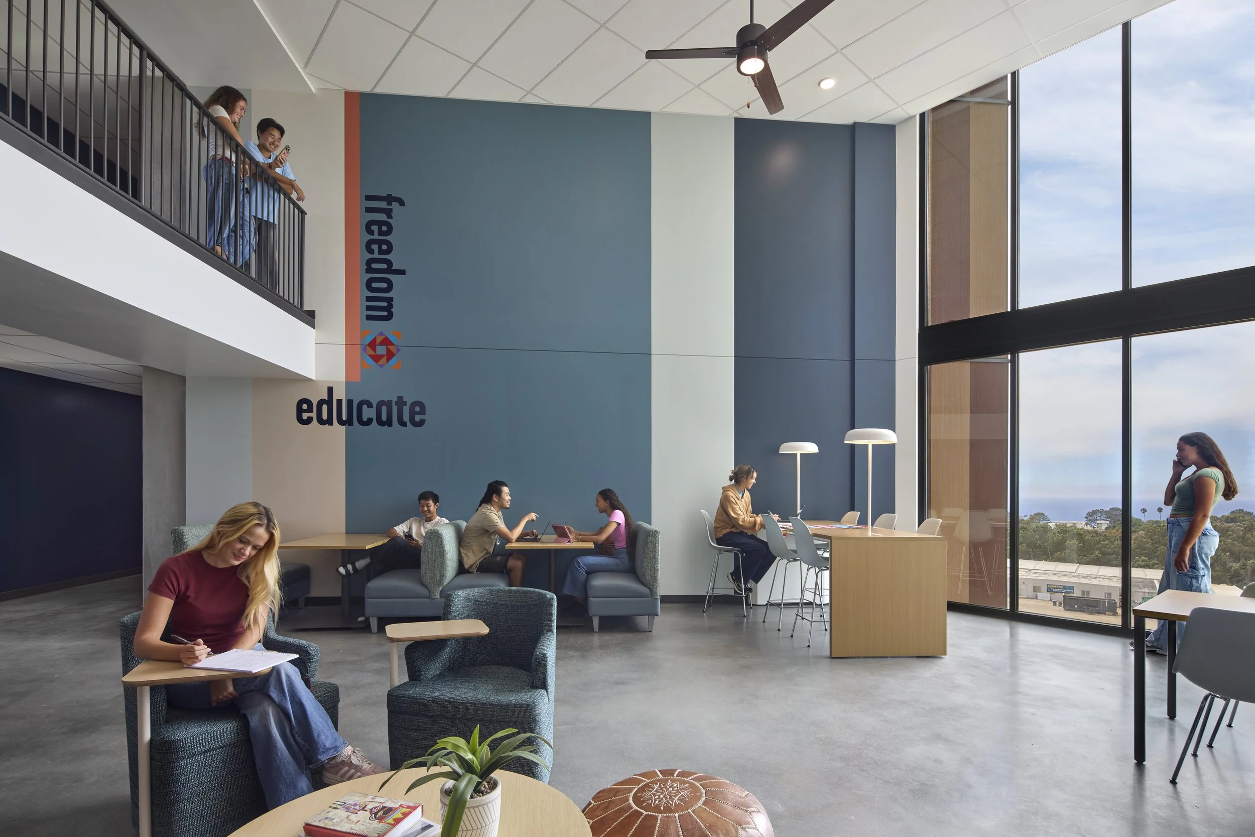People sitting and chatting in a modern, bright public space with large windows, high ceilings, and colorful interior walls that have the words 'freedom' and 'educate' written on them.