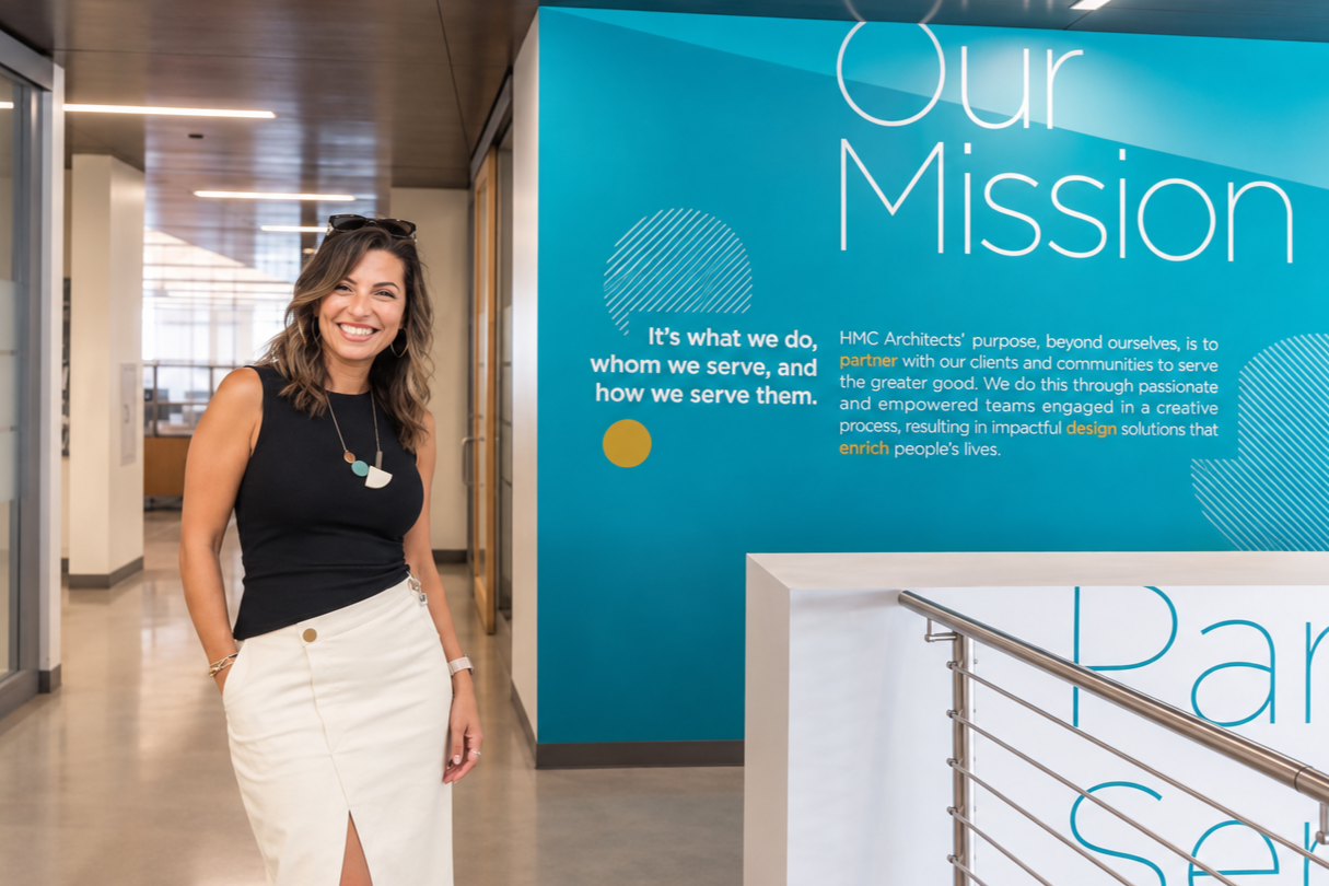 Lydia Alfred beside the Designing for Good mission statement display at HMC Architects.