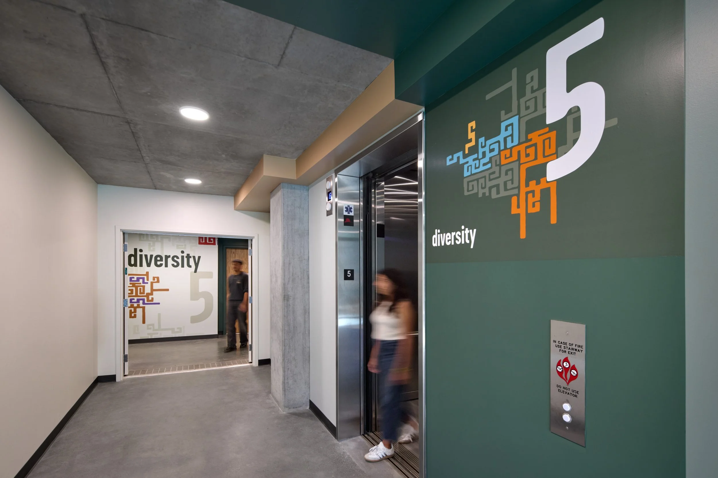 Elevator in a hallway with a mural that reads 'diversity' and colorful abstract designs.