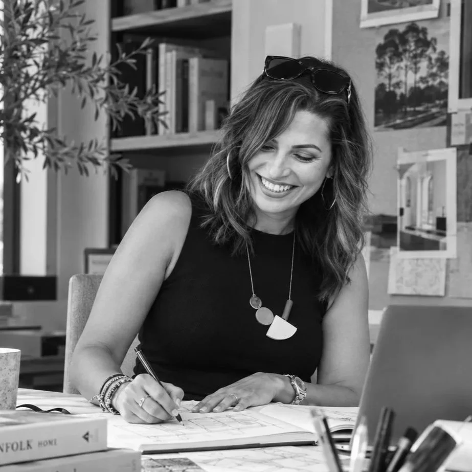 Black-and-white photograph of Lydia Alfred sketching at her desk, surrounded by books and design materials.