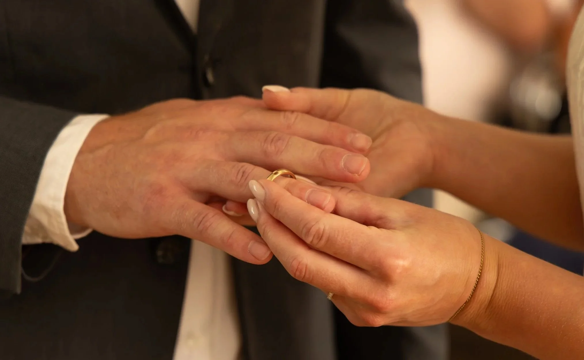 Zwei Menschen halten sich bei einer Zeremonie oder einem Vorstellungsgespräch an den Händen, eine Person trägt einen goldenen Ehering und eine andere eine dünne goldene Kette. Trauung, Standesamtliche Hochzeit, Details.
