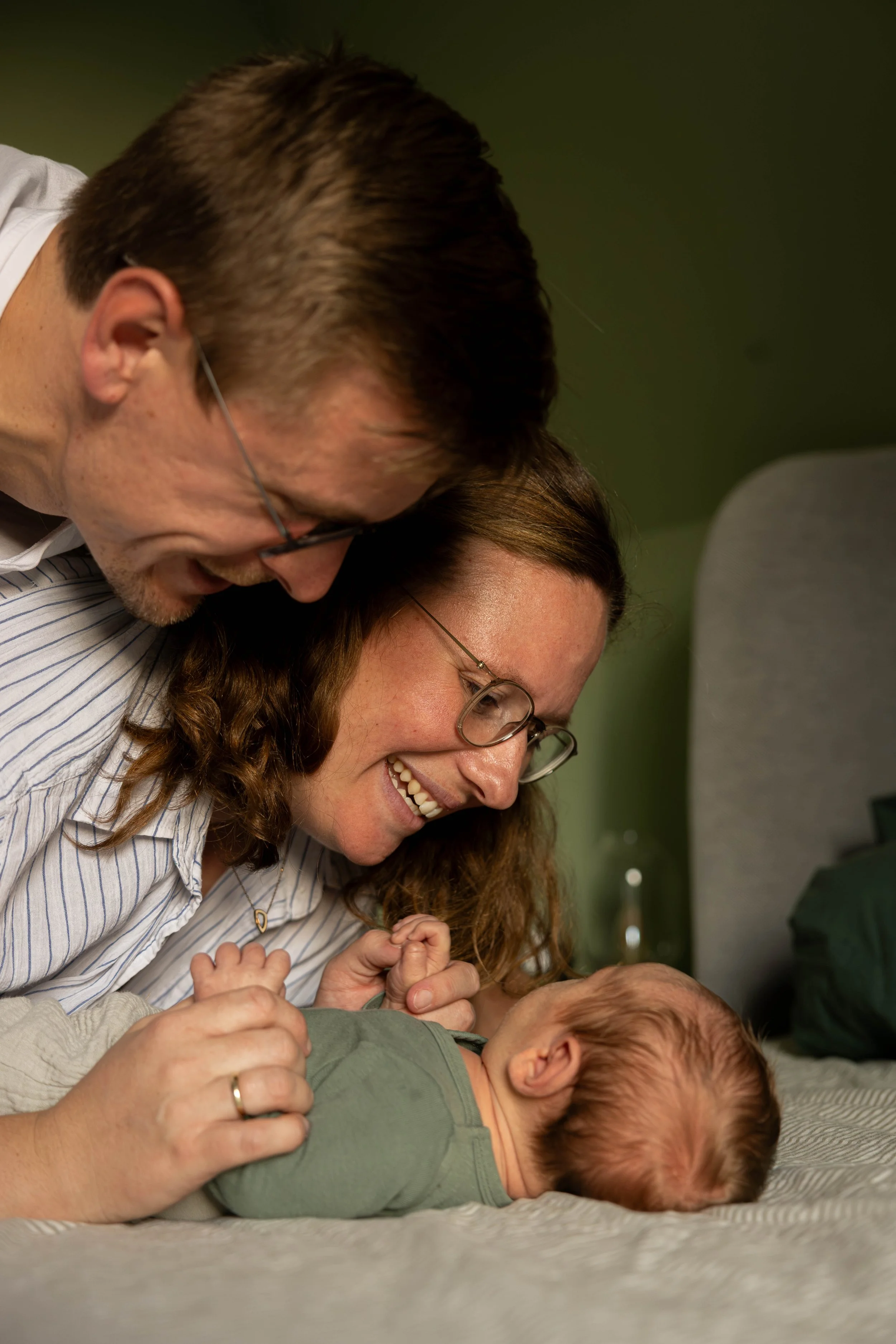 Familie spielt lachend mit Baby auf dem Boden, Innenraum mit grüner Wand im Hintergrund. Newborn, Newborn Shooting, Familien Shooting, Familie.