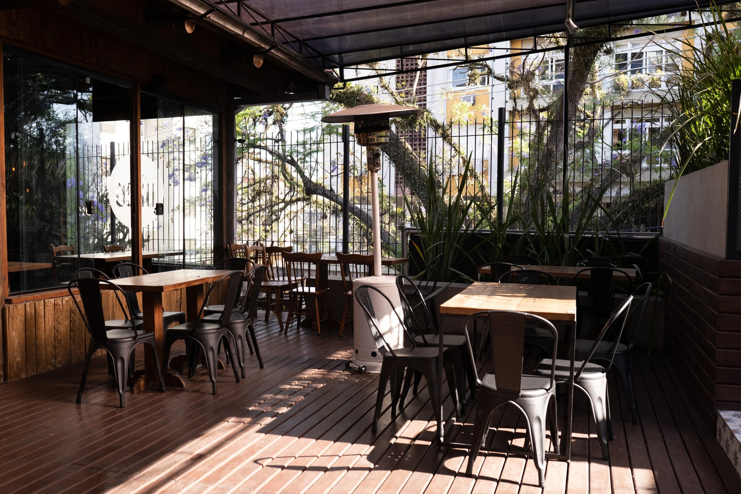 Deck coberto do Osso Parrilla Bar no Bom Fim, com mesas, cadeiras de ferro e aquecedor externo