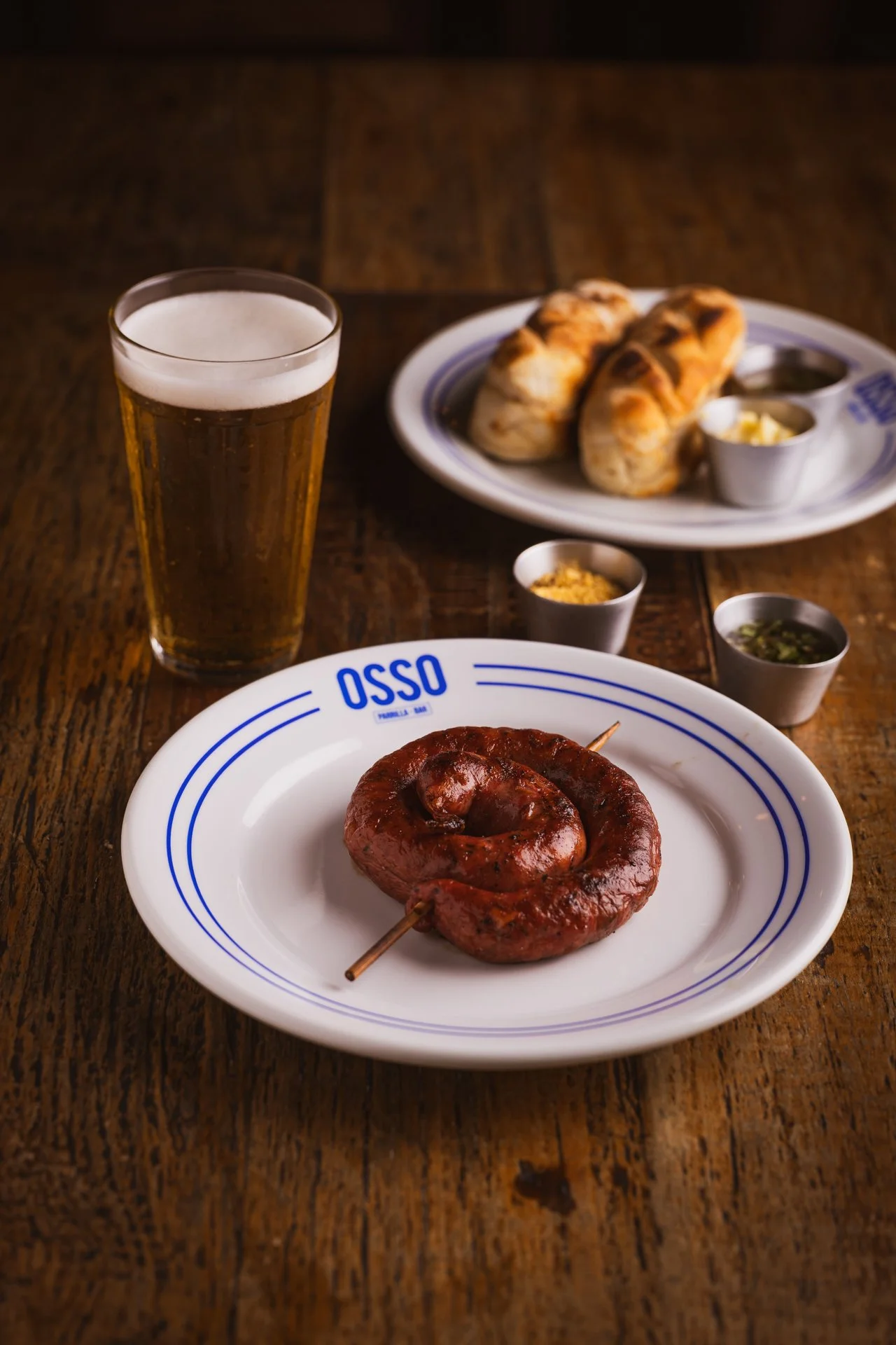 Linguiça parrillera de ovelha recheada com queijo, com pão, molhos e copo de chopp
