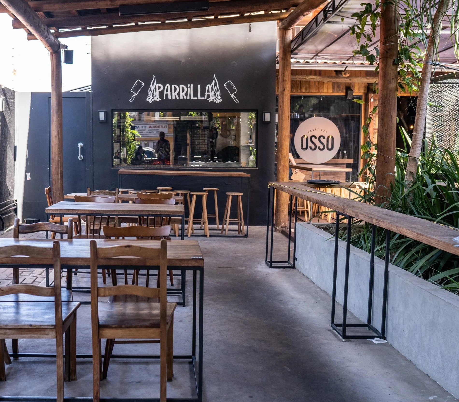 Pátio coberto do Osso Parrilla Bar no Bom Fim, com mesas de madeira e a placa "Parrilla" ao fundo