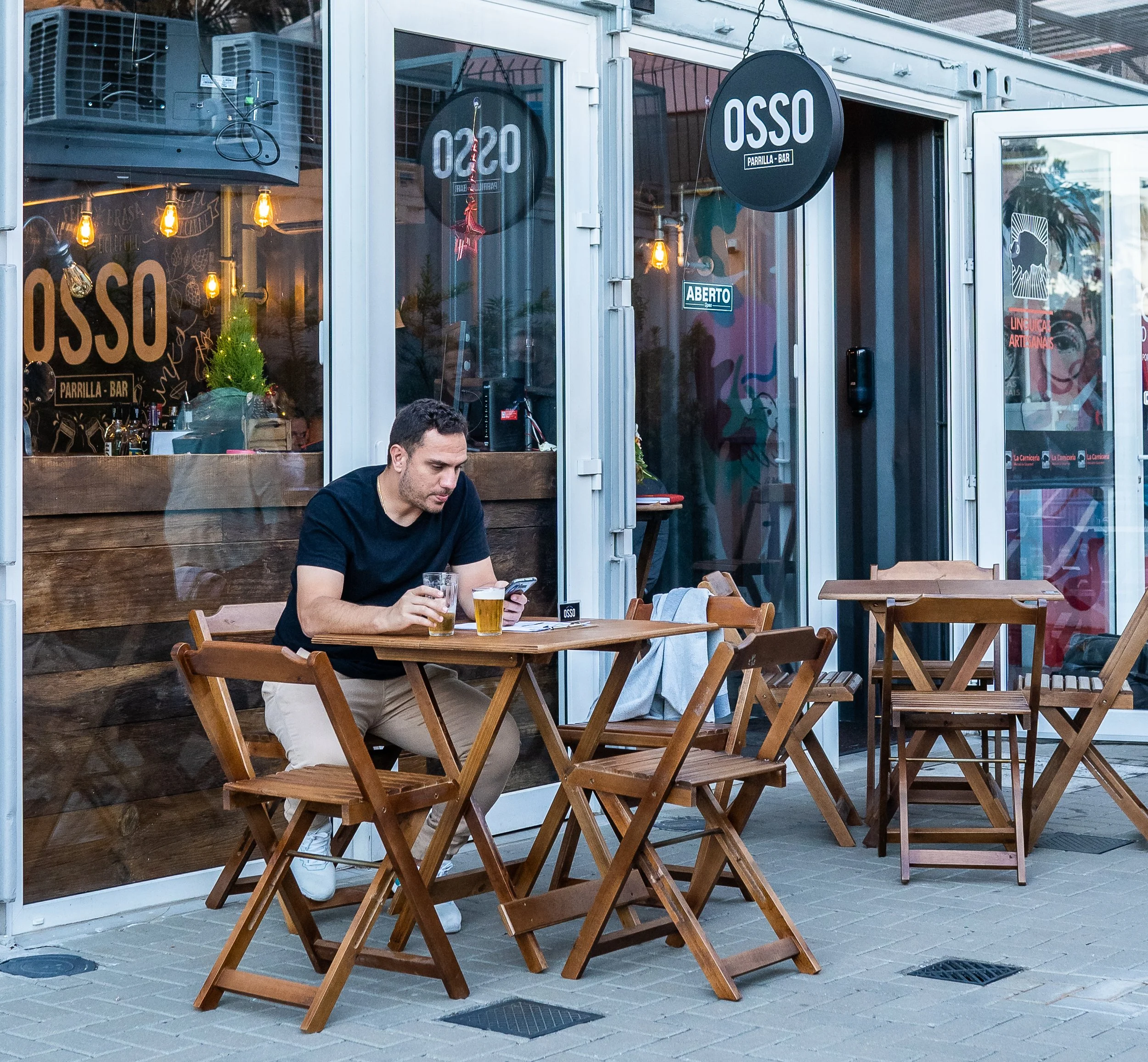 Cliente tomando cerveja em mesa de madeira na área externa do Osso Parrilla Bar em Canoas
