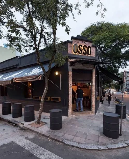 Fachada preta do Osso Parrilla Bar na esquina, na Cidade Baixa, com tambores na calçada
