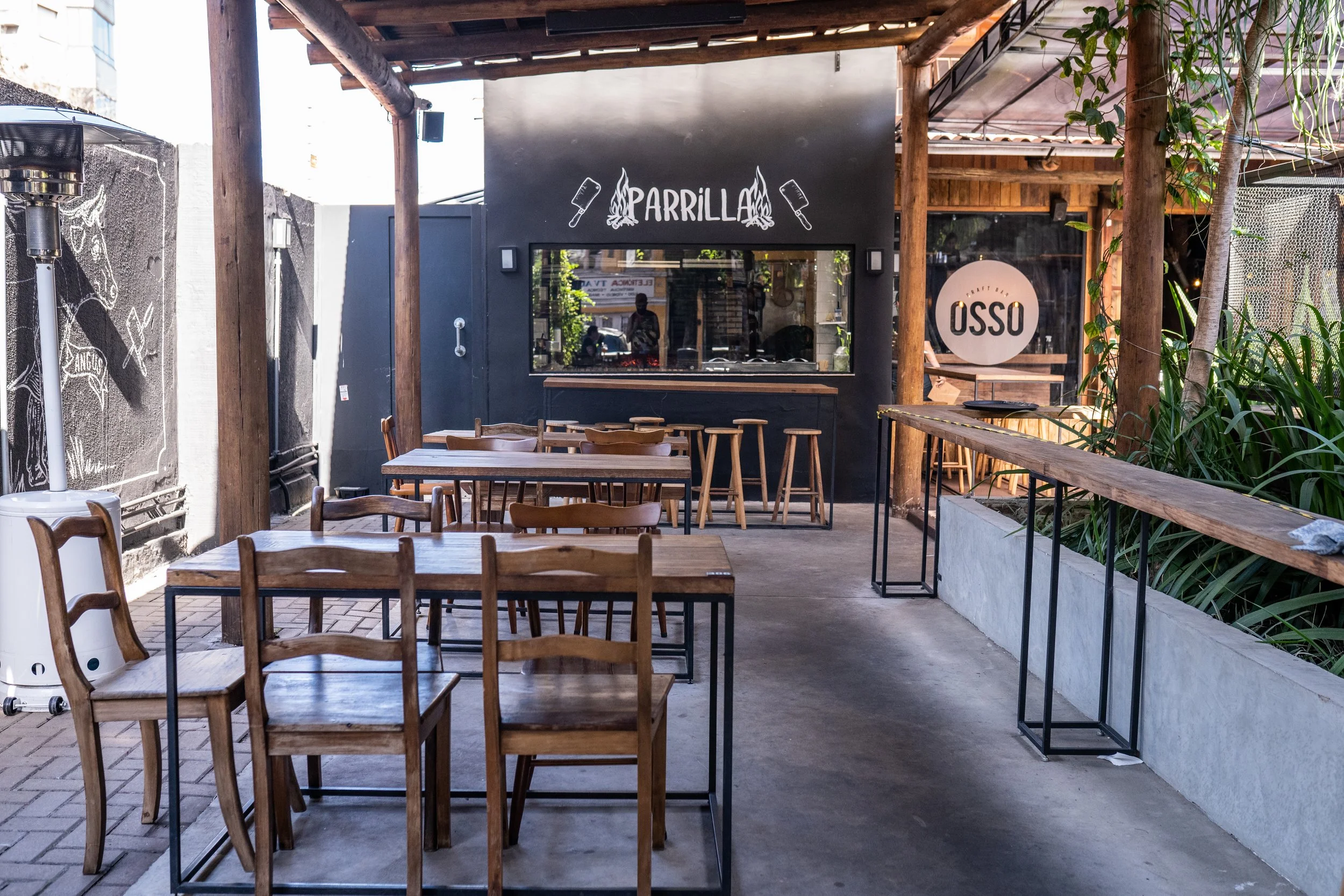 Pátio coberto do Osso Parrilla Bar no Bom Fim, com mesas de madeira e a placa "Parrilla" ao fundo