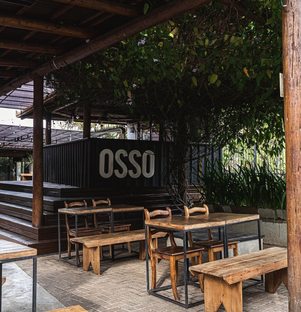 Pátio externo do Osso Parrilla Bar no Bom Fim, com mesas e bancos de madeira sob as árvores