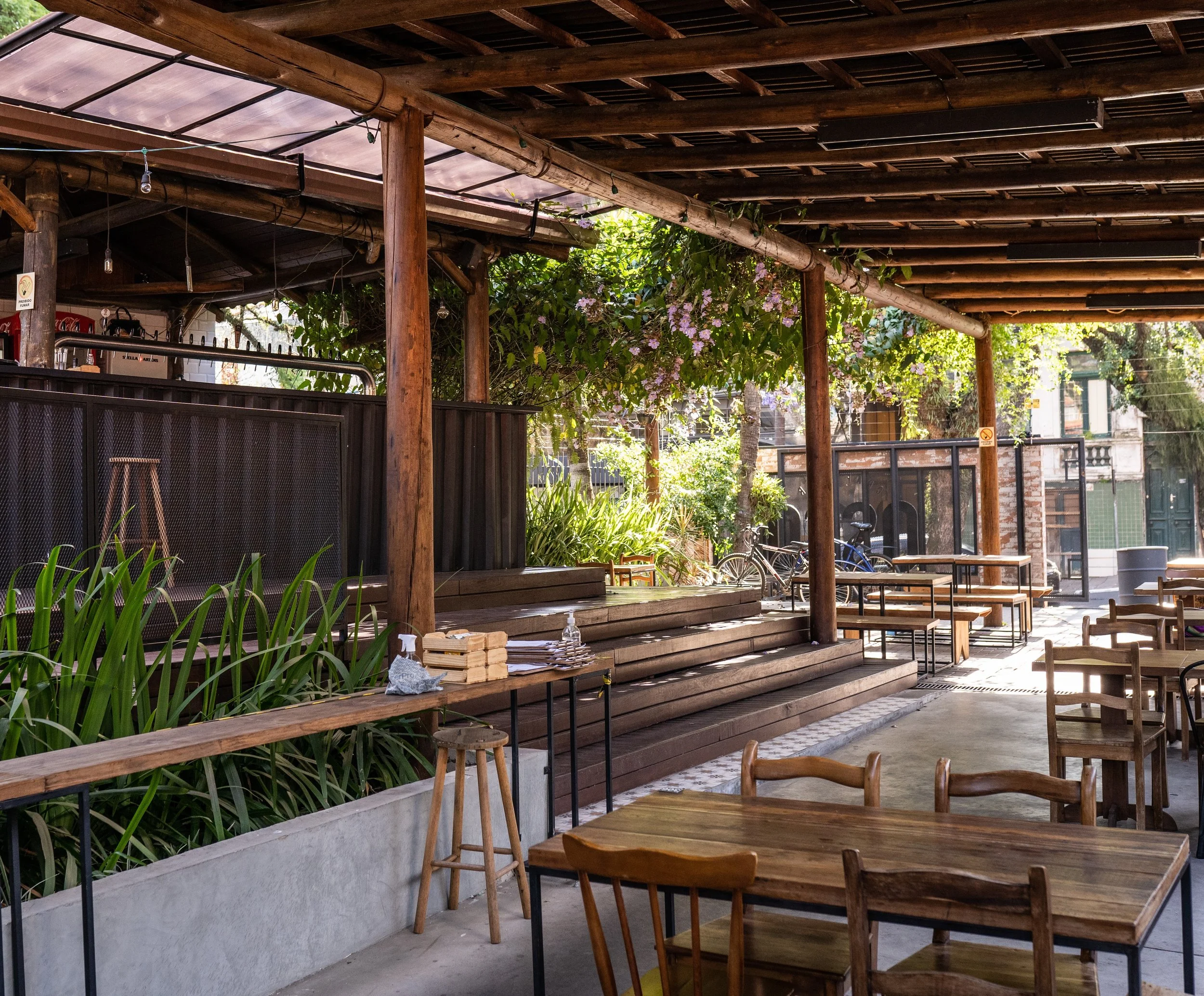 Pátio coberto do Osso Parrilla Bar no Bom Fim, com mesas de madeira e jardim ao fundo