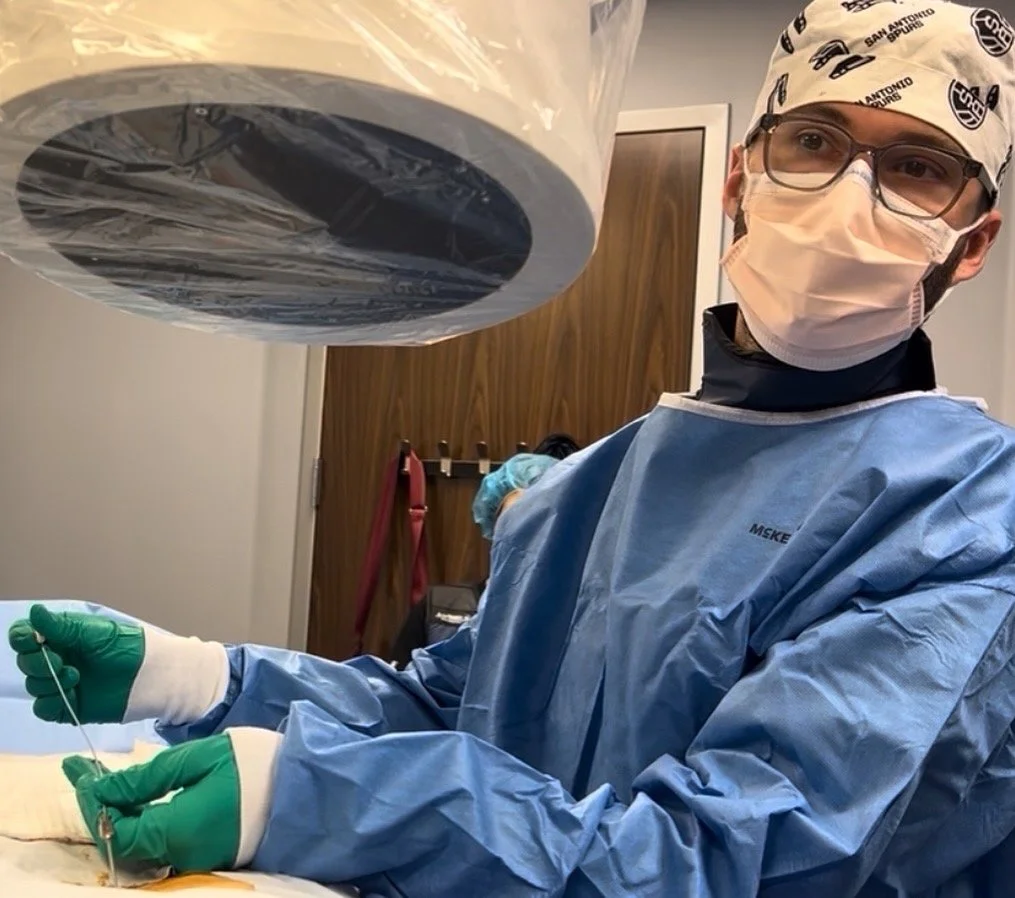 A medical professional in a surgical gown, mask, and gloves holding a syringe, performing a procedure in a sterile environment.