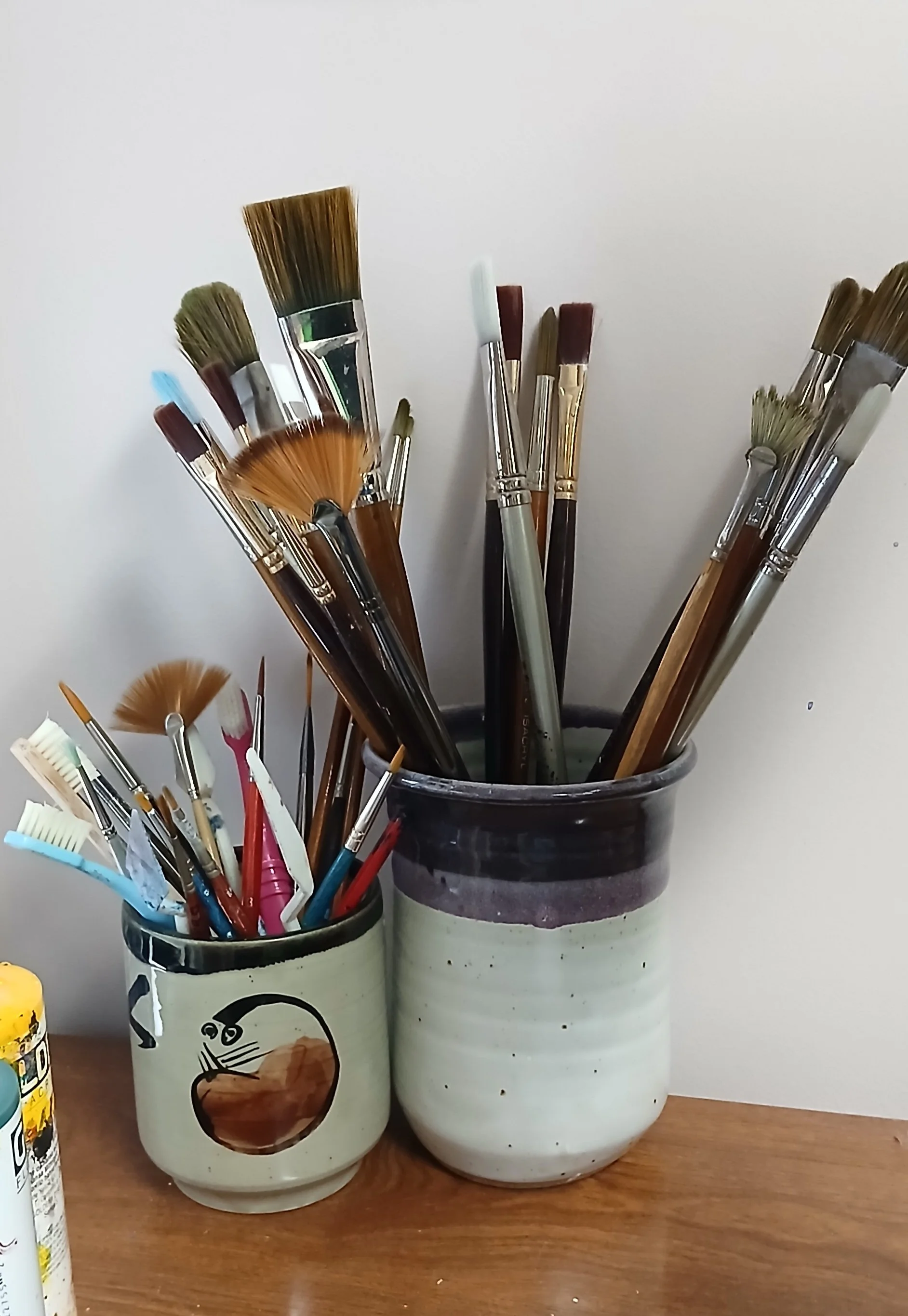 Two pottery vessels with multiple sizes of artist's paintbrushes and tools.