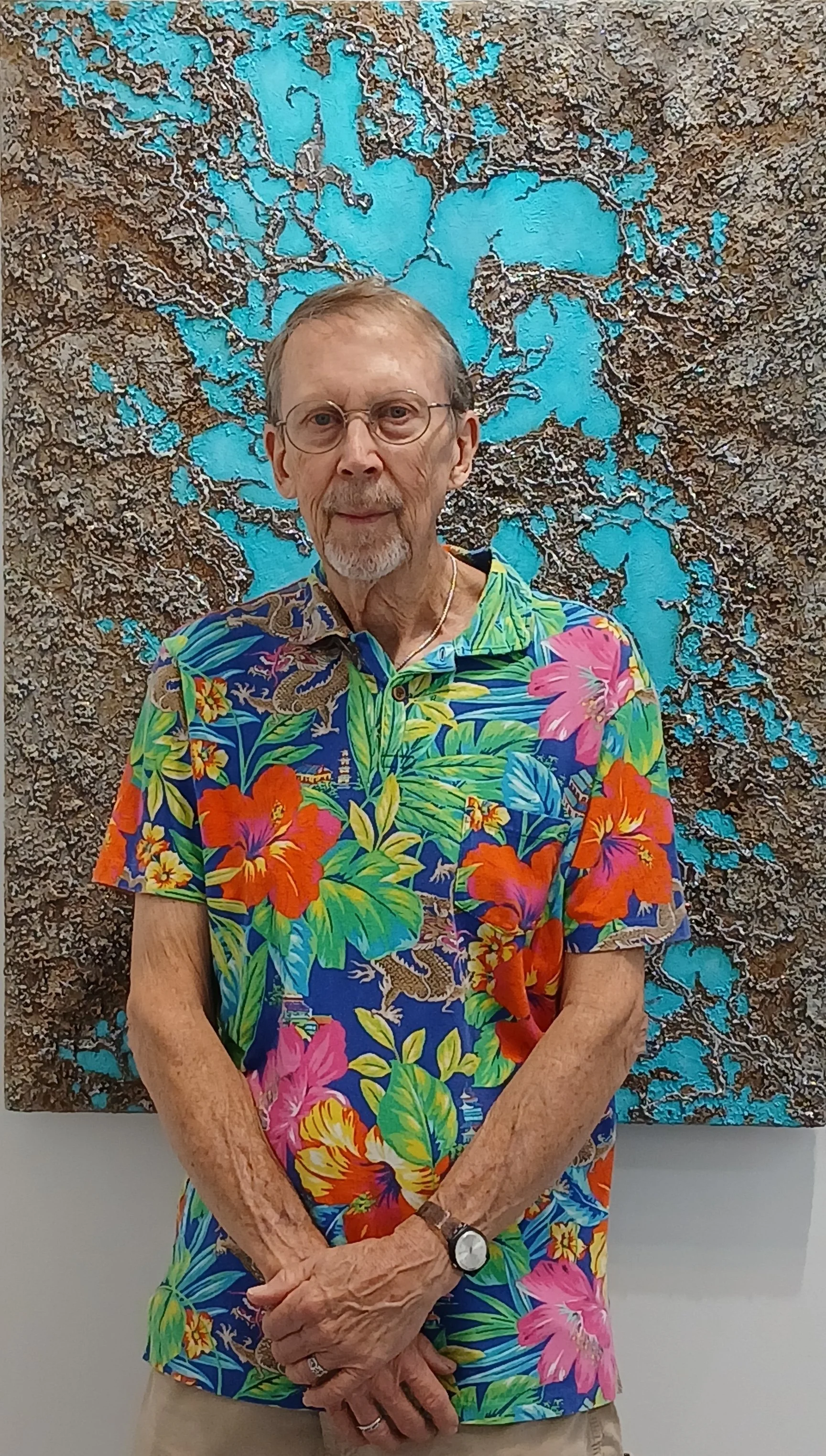 Artist Robert Gibbs in a brighly colored shirt standing in front of his abstract painting Turquoise.