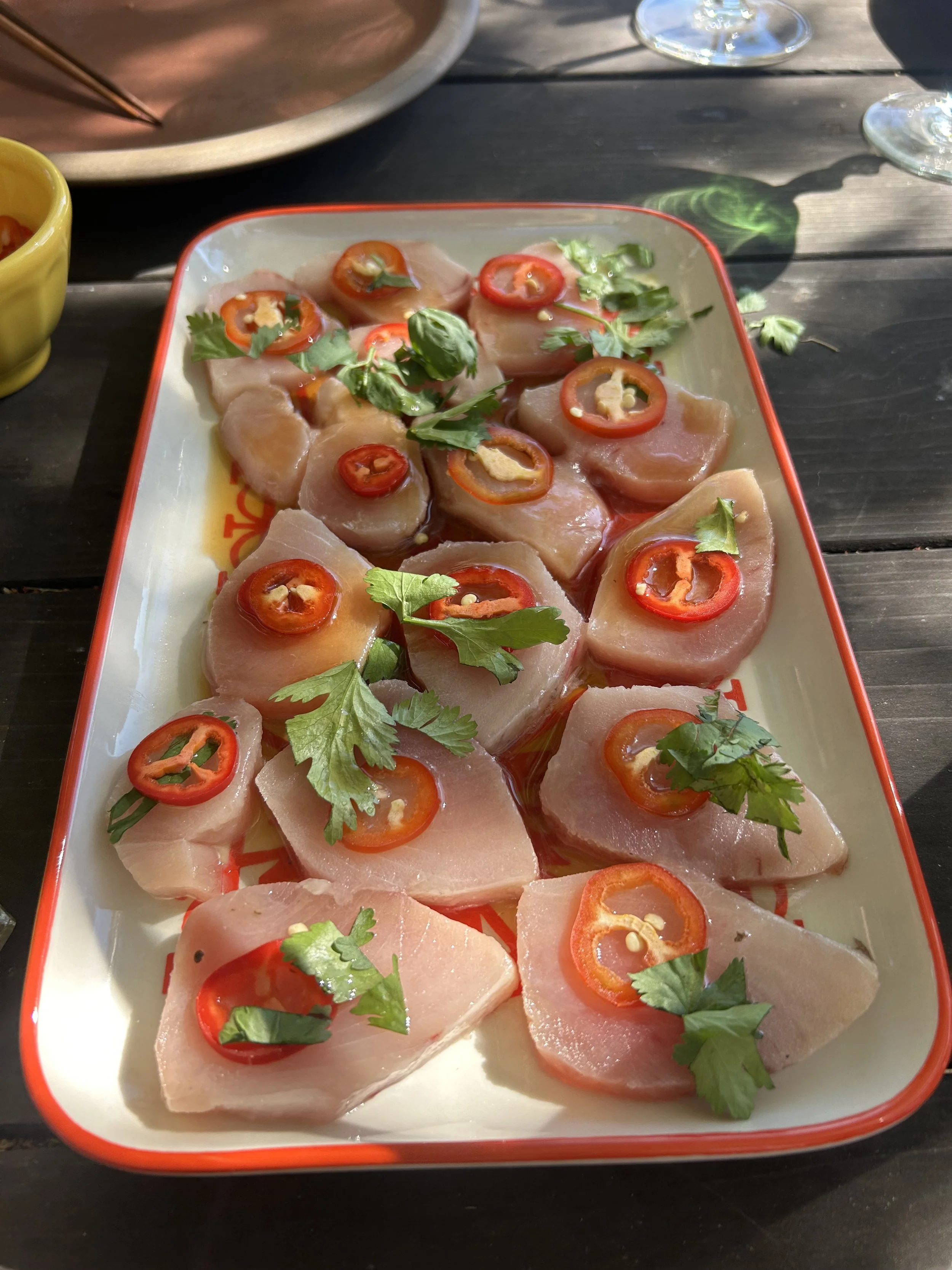 Thin slices of raw fish topped with sliced red chili peppers and fresh cilantro on a rectangular white plate with a red rim.
