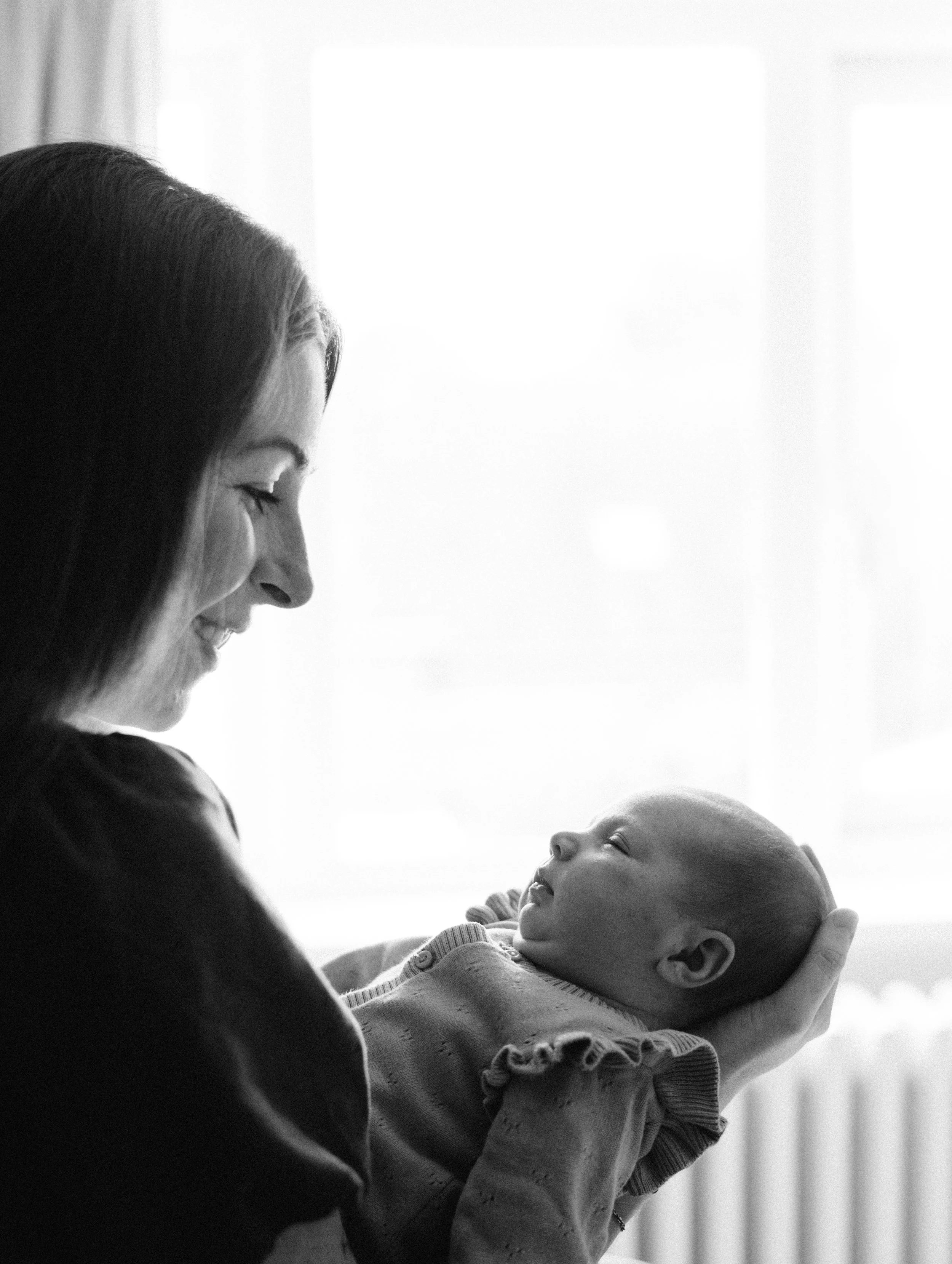 A woman and a baby sharing a moment of joy, with the woman smiling and the baby looking at her, in black and white.