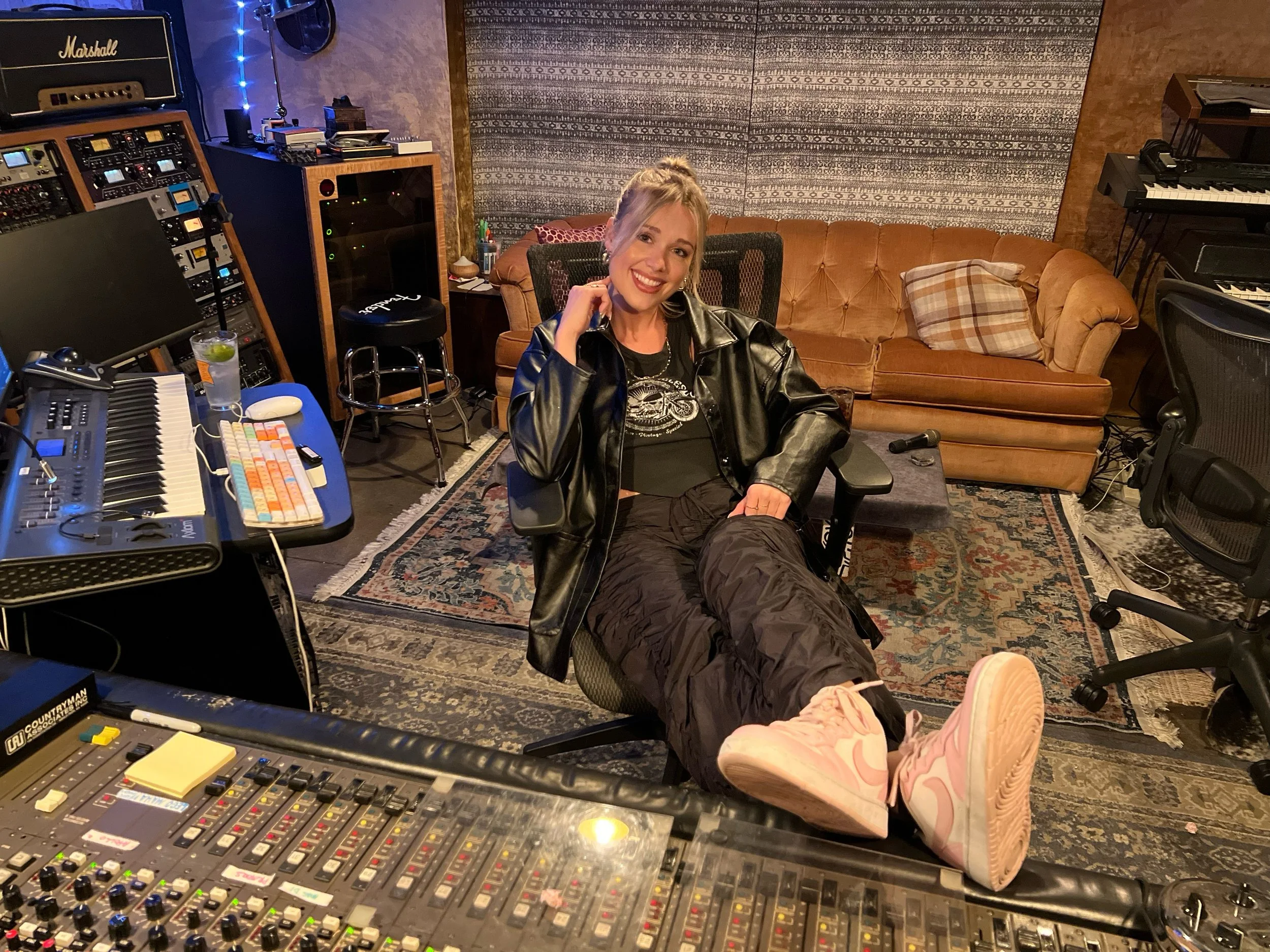 Singer-songwriter Paige Corwin in a recording studio surrounded by music production equipment.