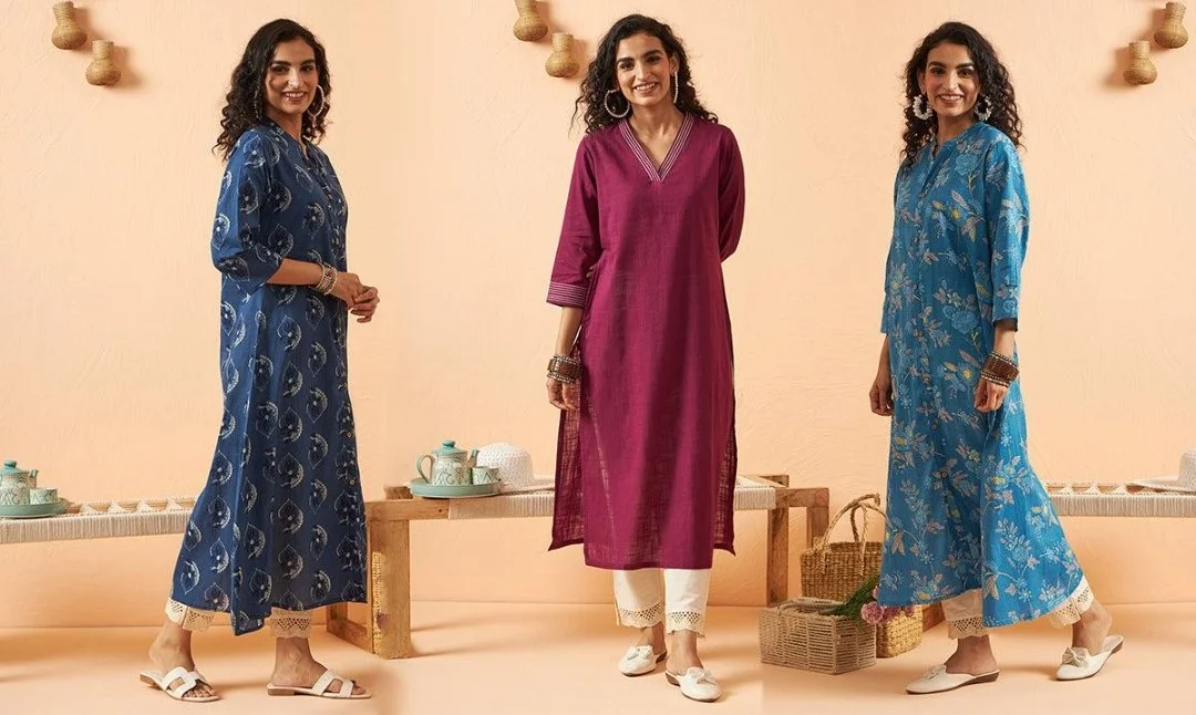 Three women in colorful traditional Indian dresses standing against a beige background with hanging woven decorations.
