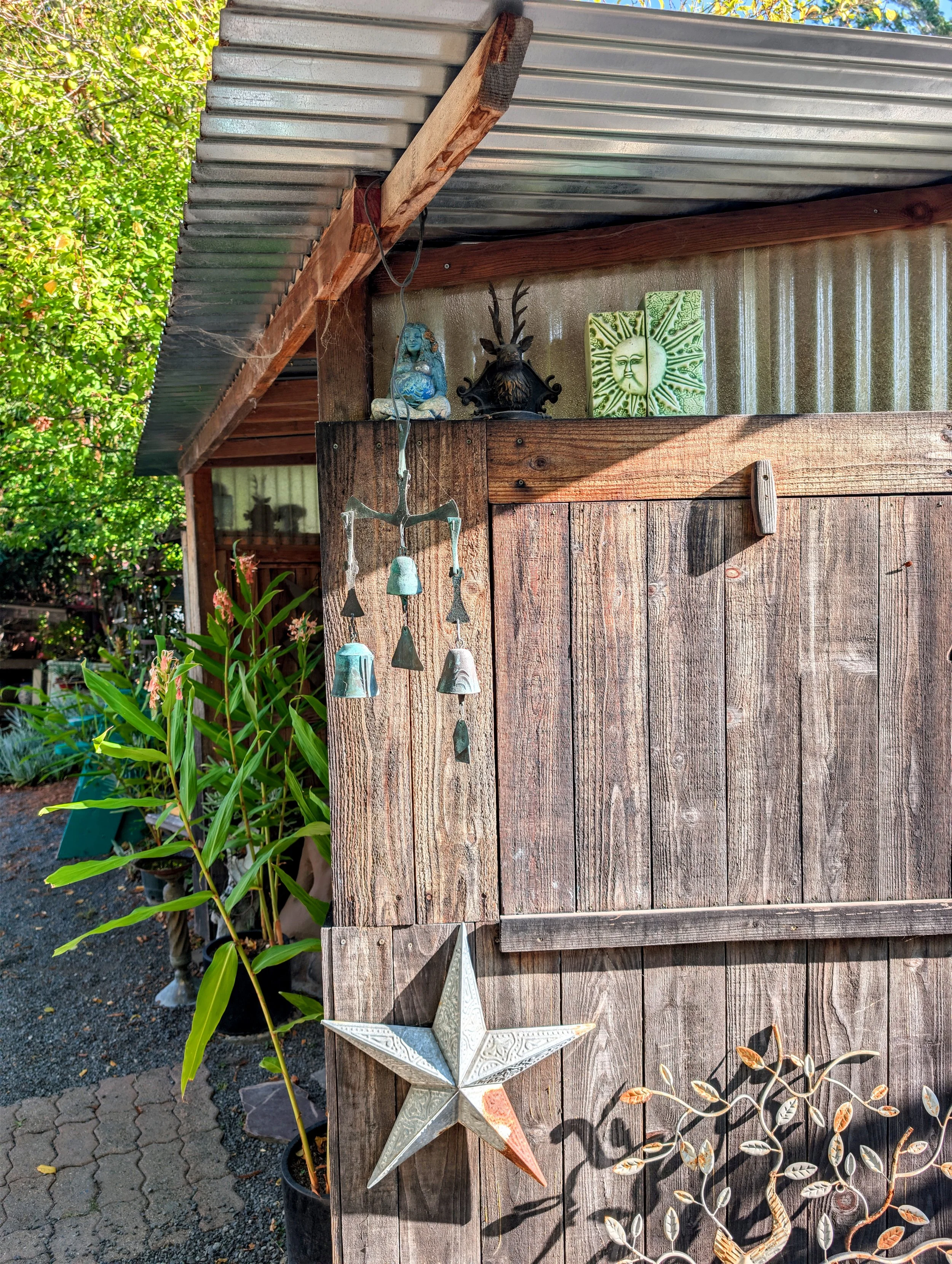 Decorative outdoor scene with a wooden fence, greenery, a star-shaped ornament, small statues, and a wall with textured tiles featuring a sun and moon design.