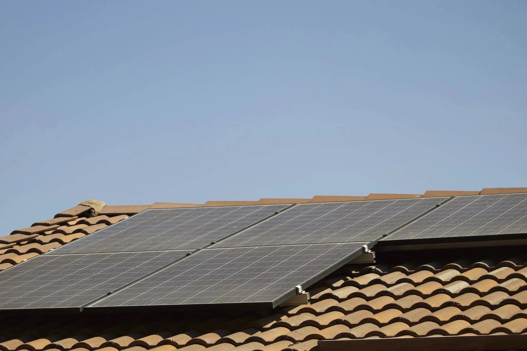 Dirty solar panels installed on a tiled roof under a clear blue sky.