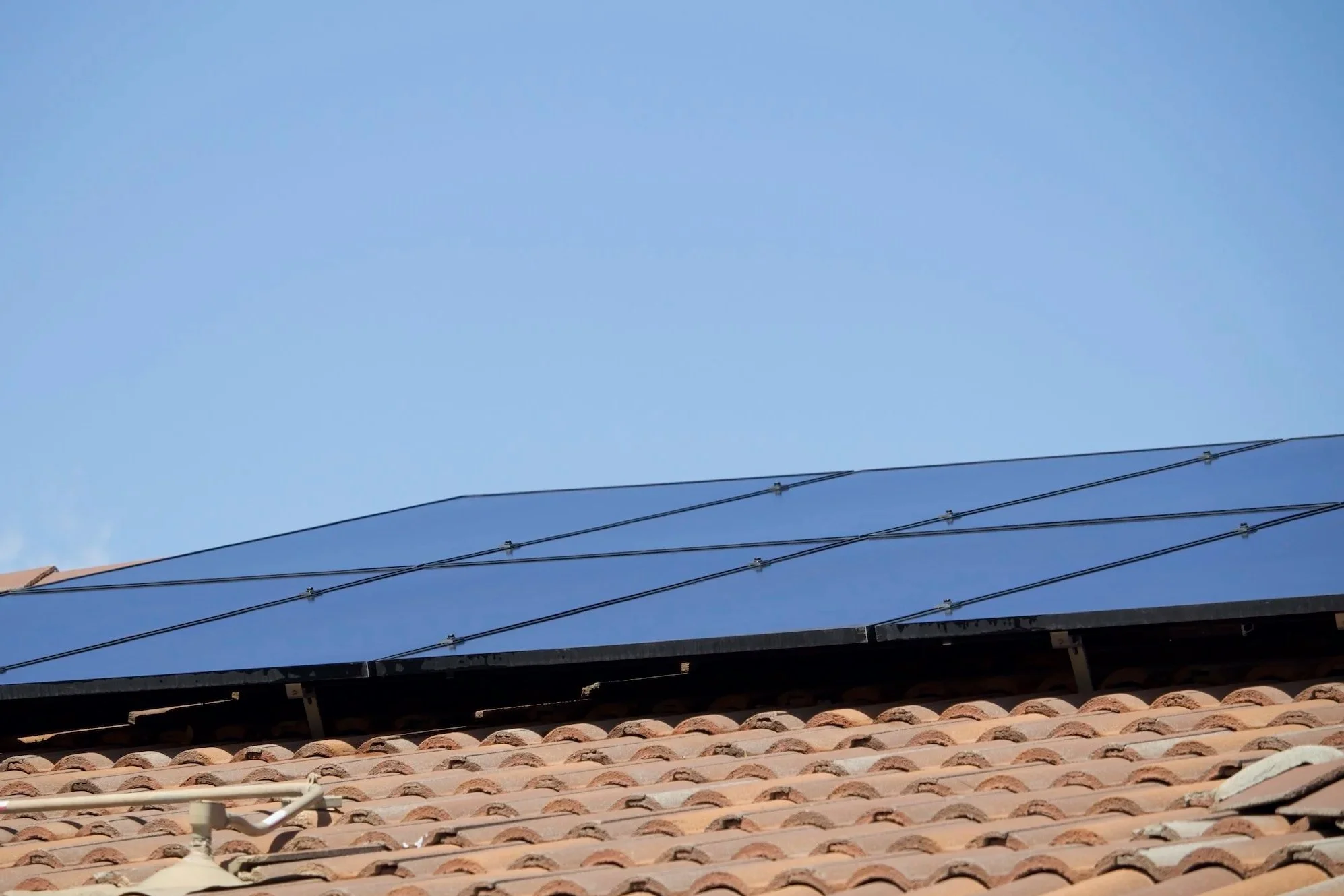 View of rooftops with clean solar panels and utility lines under a clear blue sky.