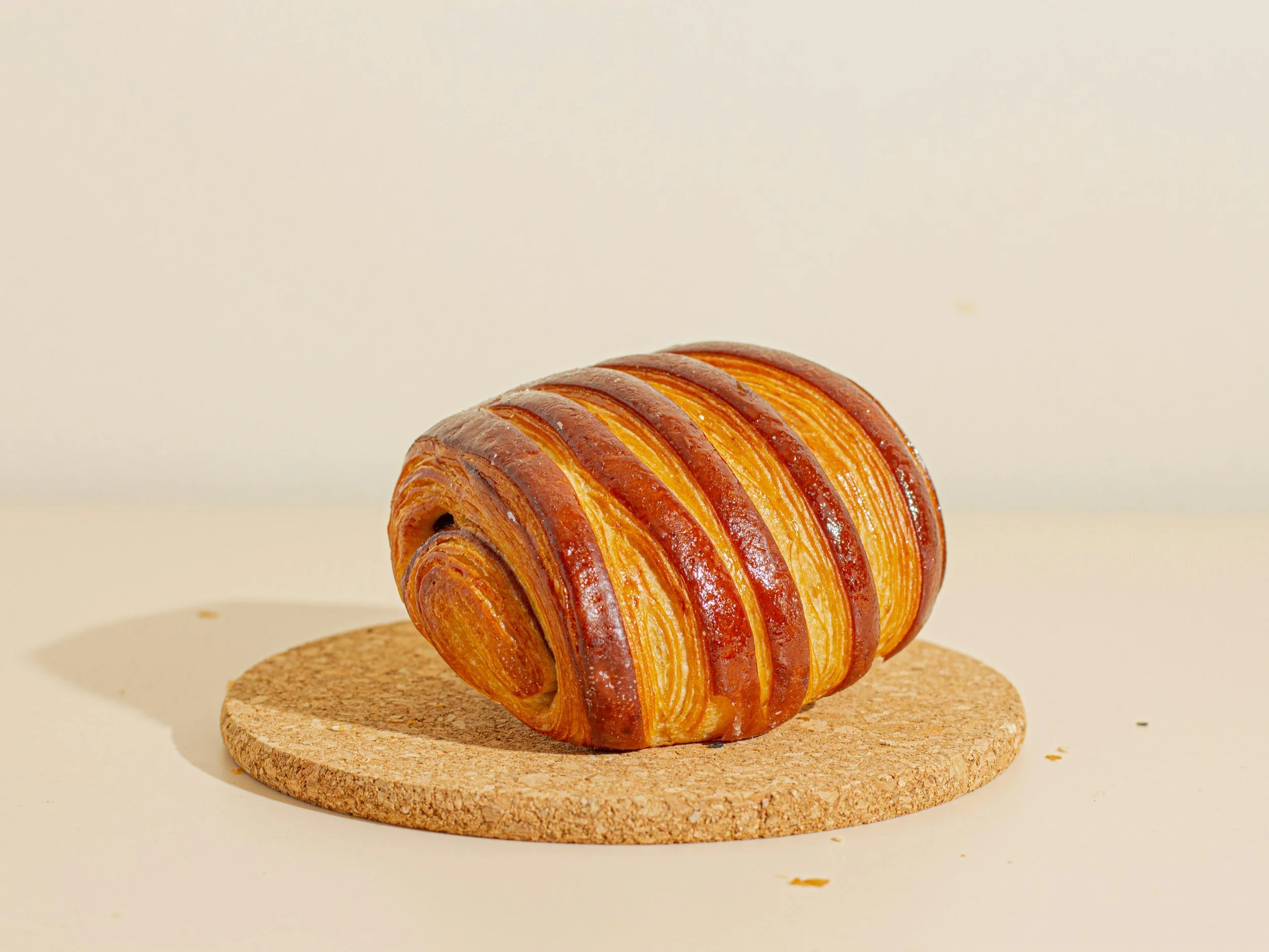A sliced, spiral pastry with a glossy, caramelized top, placed on a round cork coaster.