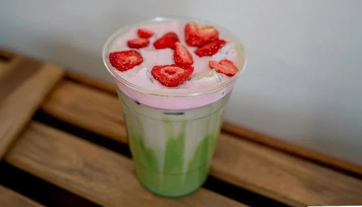 A milkshake with green and pink swirls topped with sliced strawberries on a wooden surface.