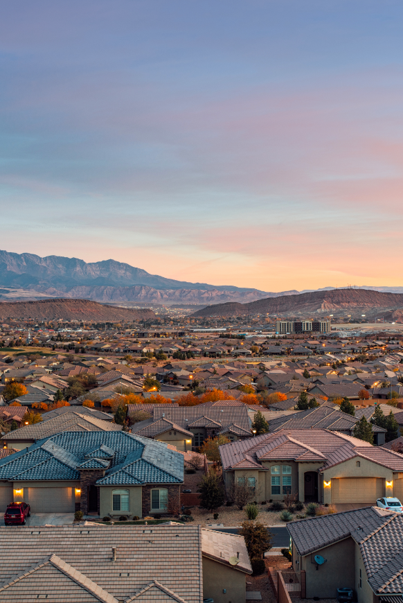 Suburban neighborhood with houses, trees, and mountains in the background during sunset.
