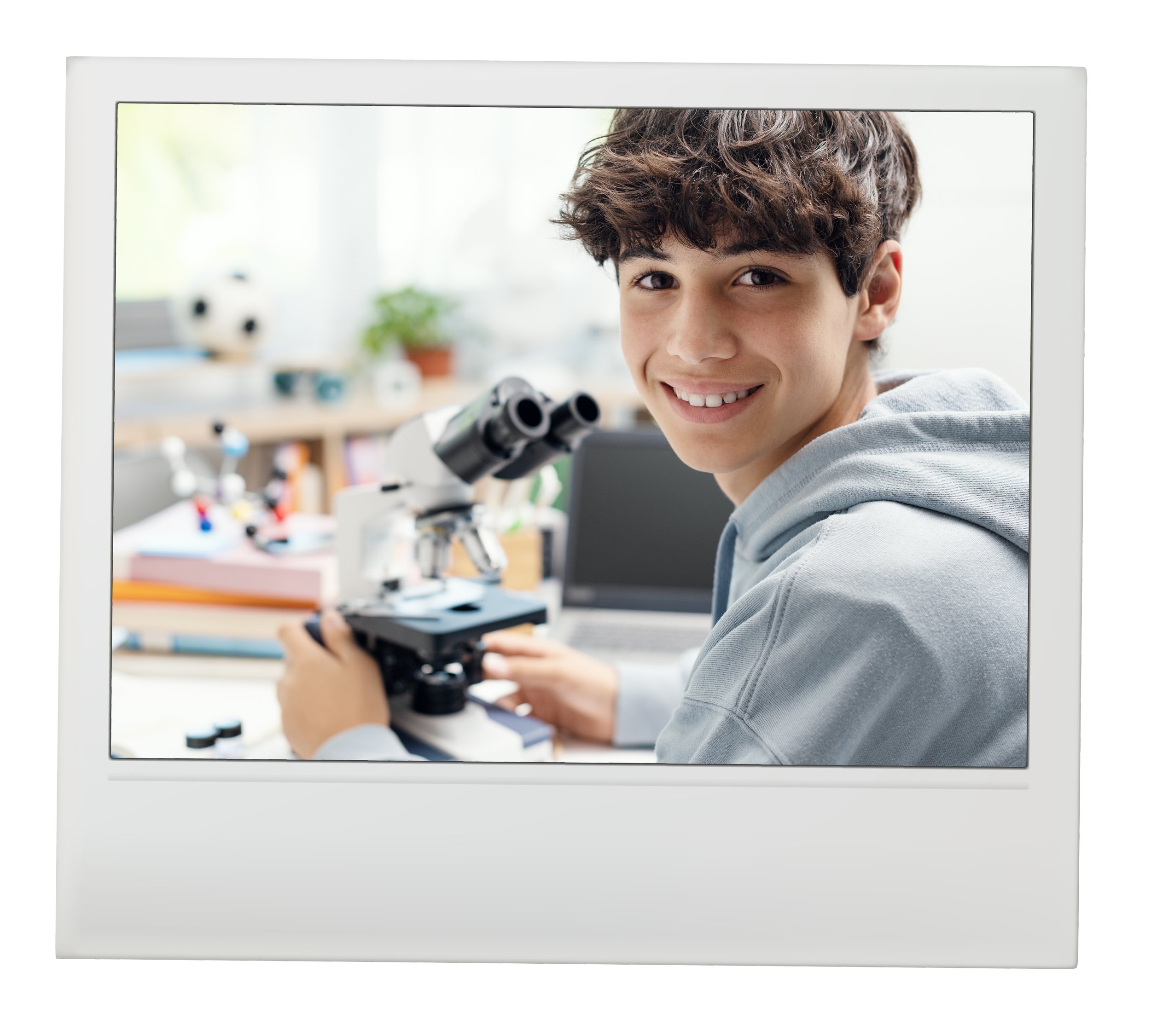Young boy with curly brown hair smiling, seen through a computer monitor with a chessboard and microscope in the background.