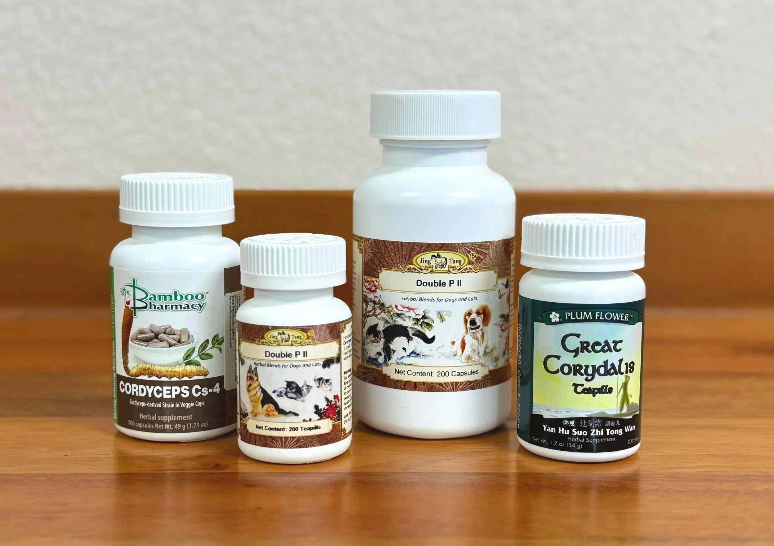 Several bottles of herbal supplements, featuring brands like Bamboo Pharmacy, Jing Tang Double P II, and Yan Hu Suo Zhi Tong Wan, placed on a wooden surface against a plain wall.