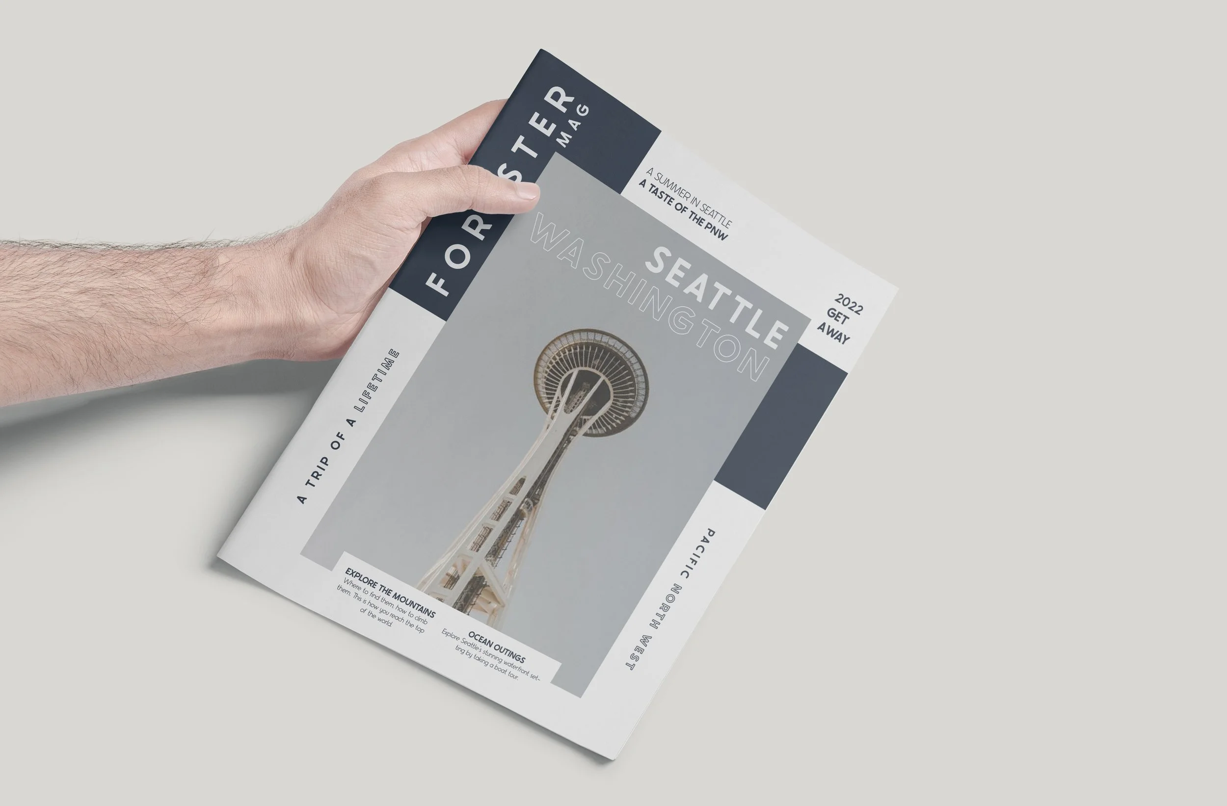 Hand holding a Seattle Seattle magazine featuring the Space Needle on the cover, with text about Seattle attractions on a light gray background.