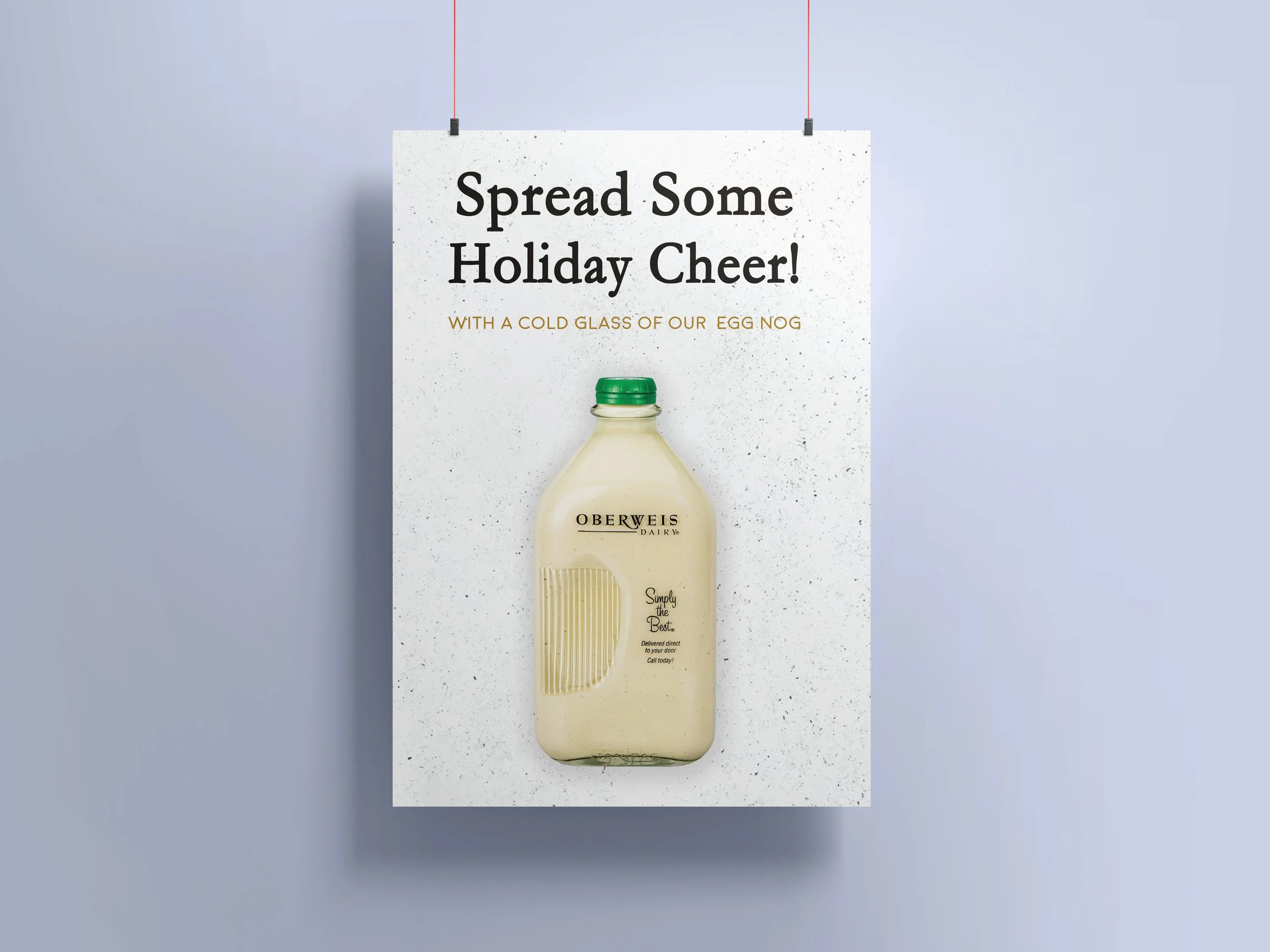 A sign with the text "Spread Some Holiday Cheer!" and a smaller line that says "With a Cold Glass of Our Egg Nog," hanging on a wall. Below the sign is a bottle of Oberweis Dairy egg nog.