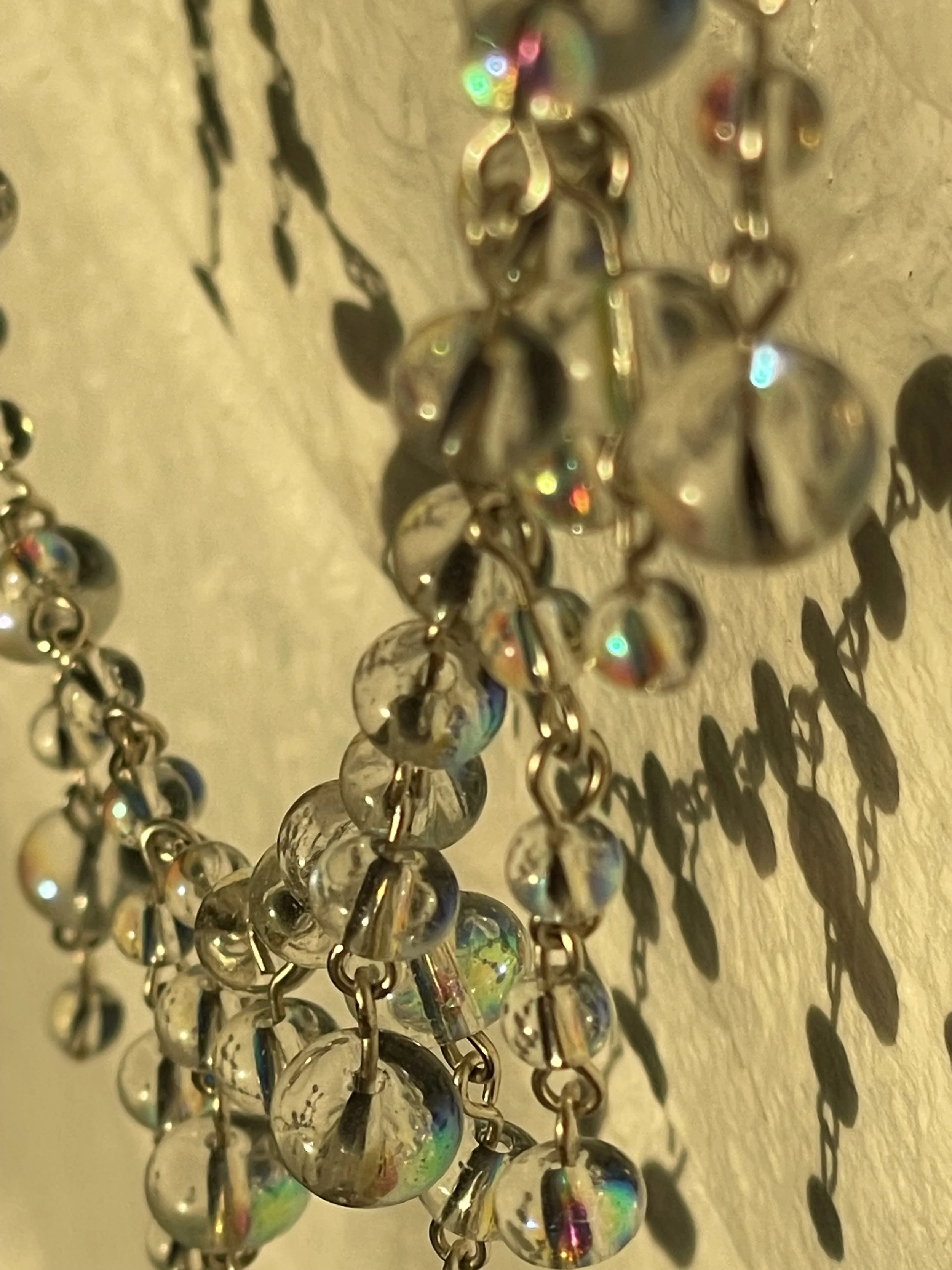 Close-up of reflective, spherical beads on a string, casting shadows on a beige surface.