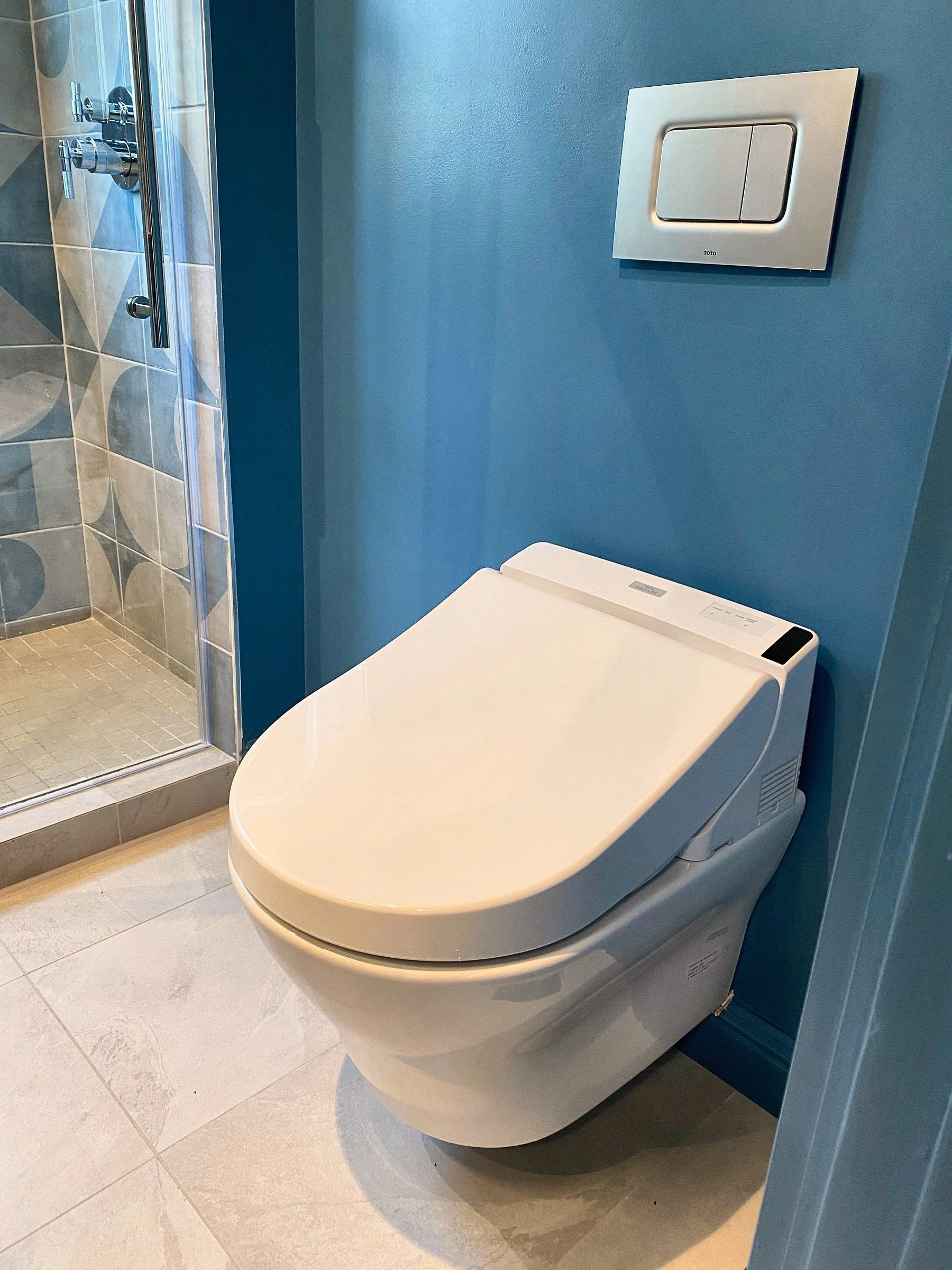Wall-hung toilet against a blue accent wall in a bathroom remodel