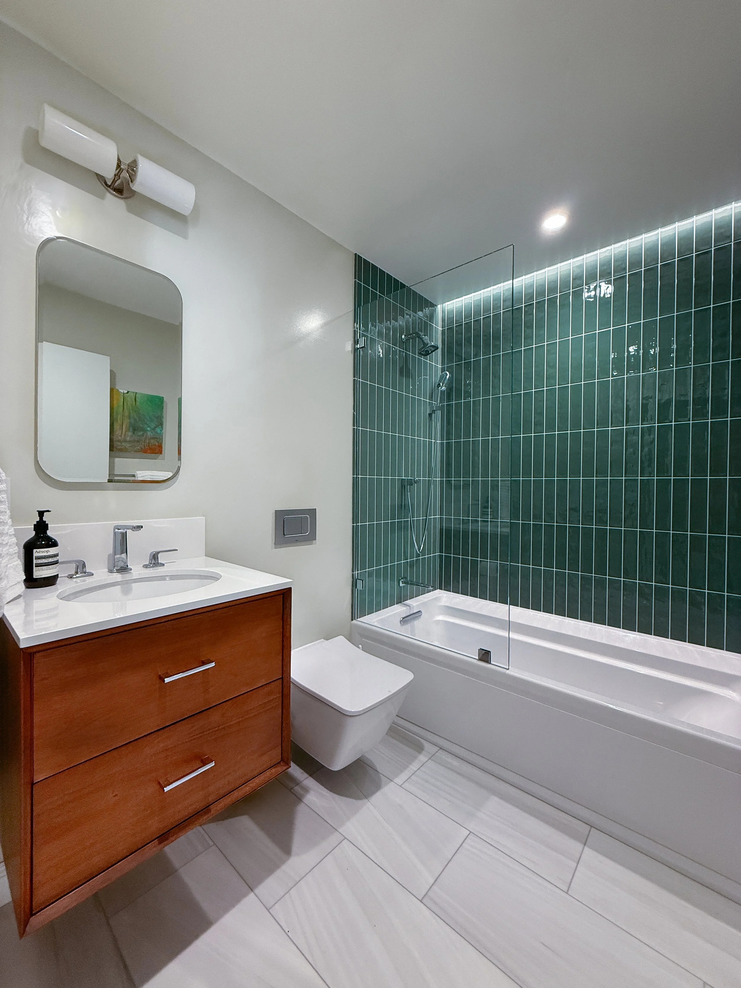 Bathroom remodel with green vertical tile, floating walnut vanity and soaking tub