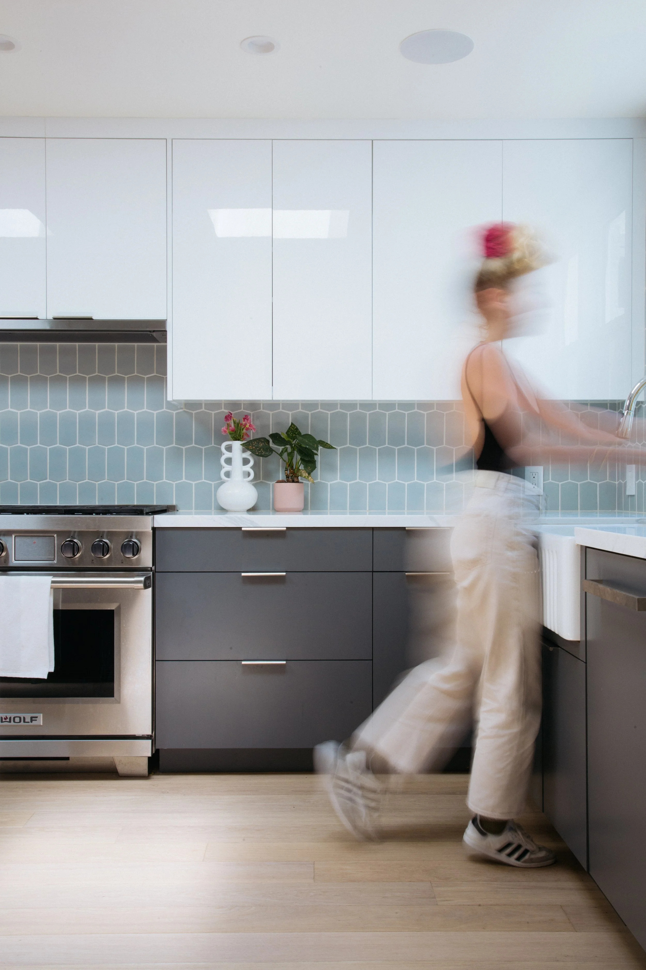 Remodeled kitchen with gray cabinets and blue hex tile, with a person walking through