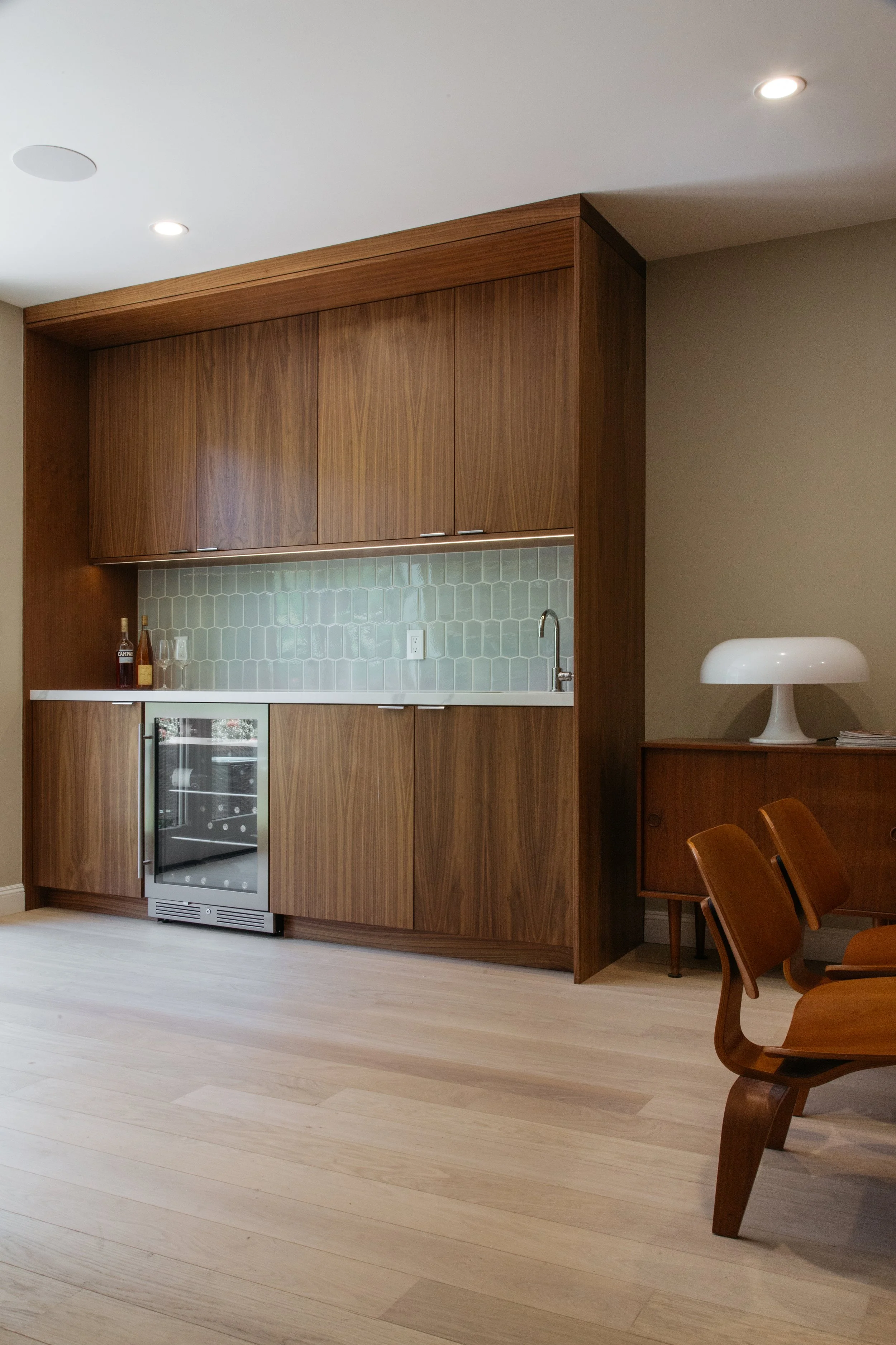 Walnut wall cabinetry with built-in wine fridge and glass tile backsplash