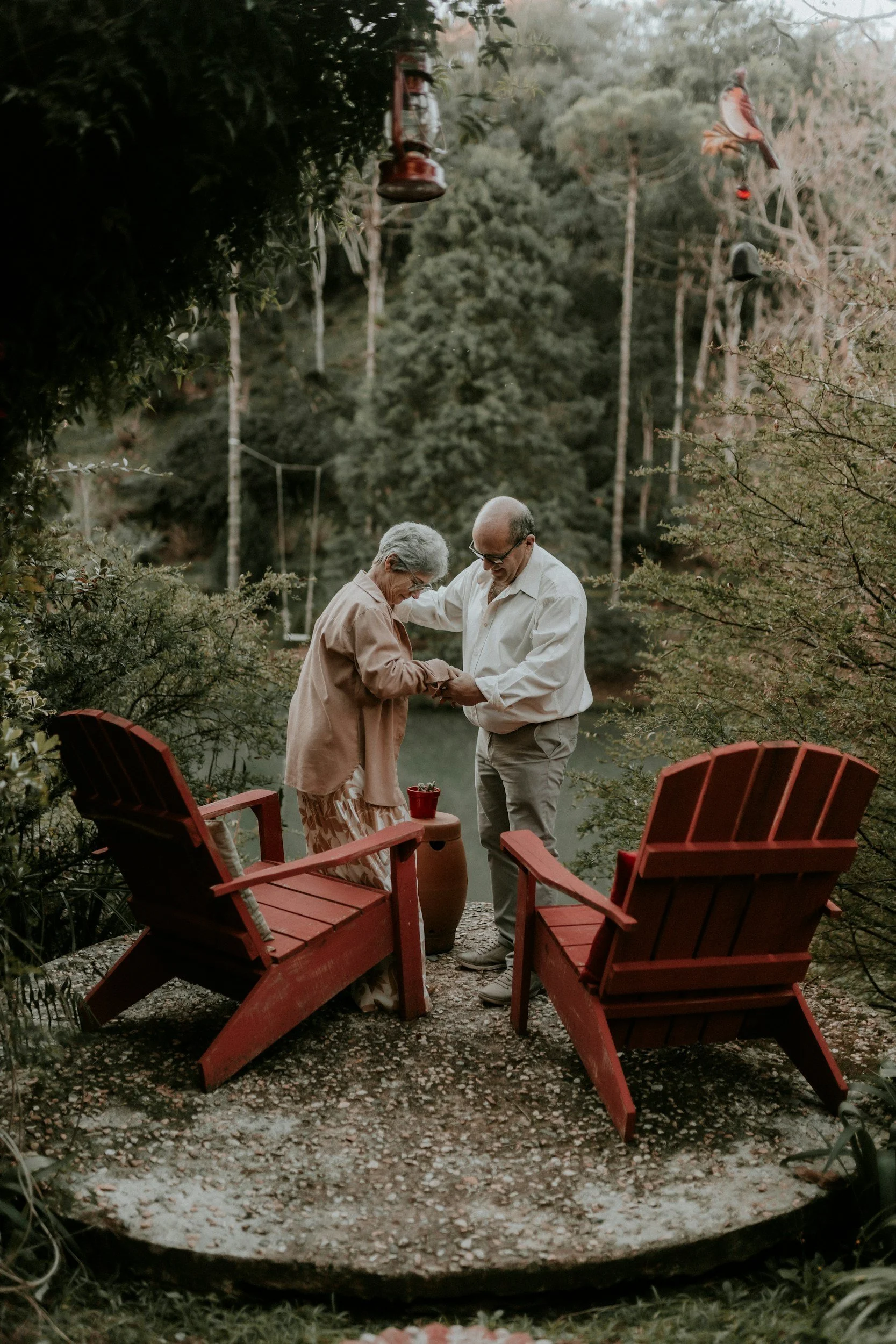 Older couple smiling and holding hands outdoors in a peaceful garden setting.